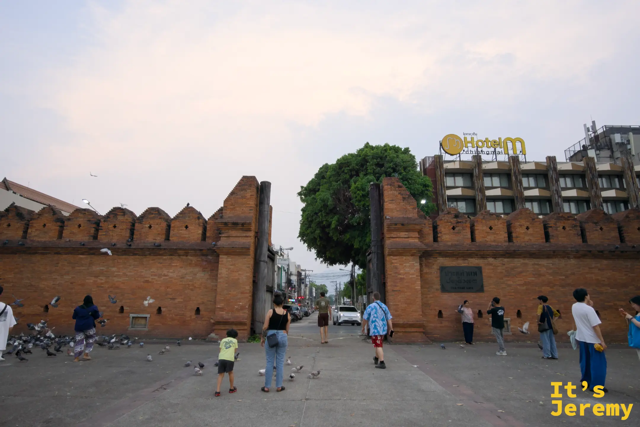 傍晚，塔佩門廣場，天空帶著粉橘色彩霞，遊客在城門前悠閒走動餵鴿