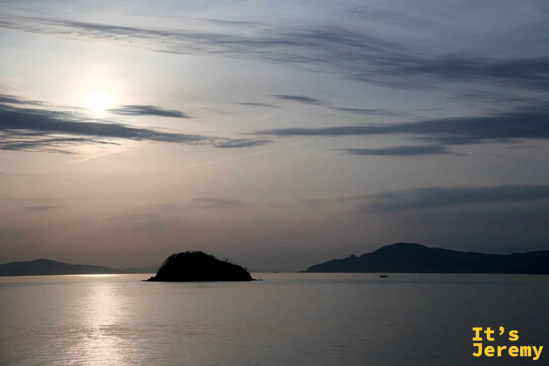 瀨戶內海傍晚景色，夕陽從雲層後透出，海面呈金橙色，中央一座島嶼剪影
