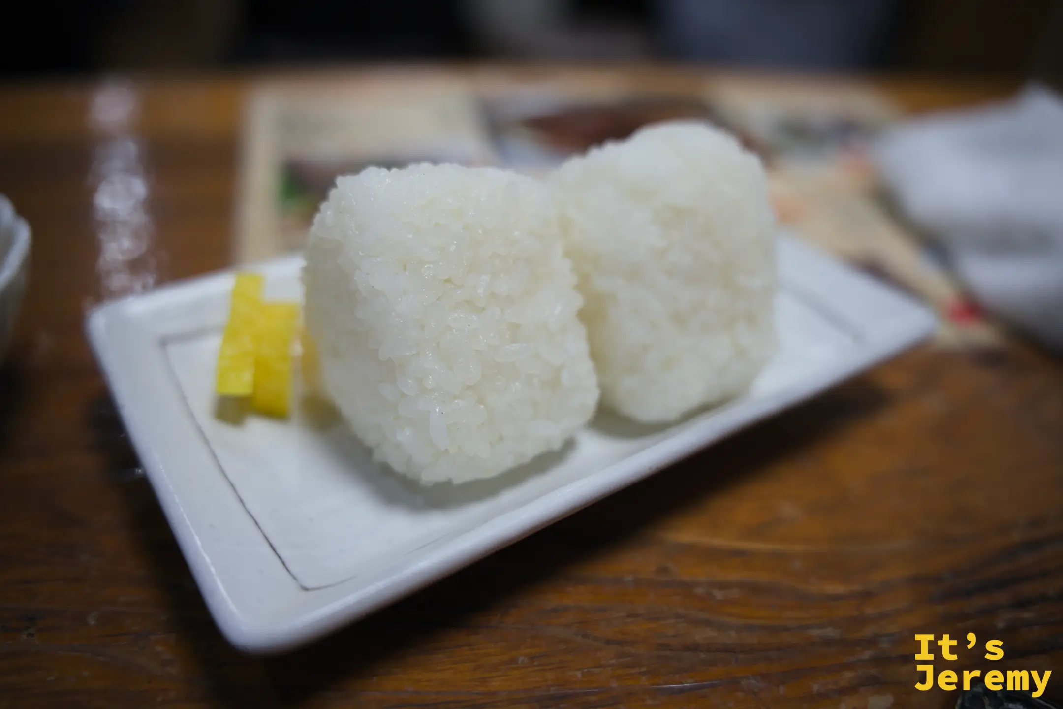 塩むすび 兩顆擺在白色長盤上，旁邊是黃色醃漬小菜