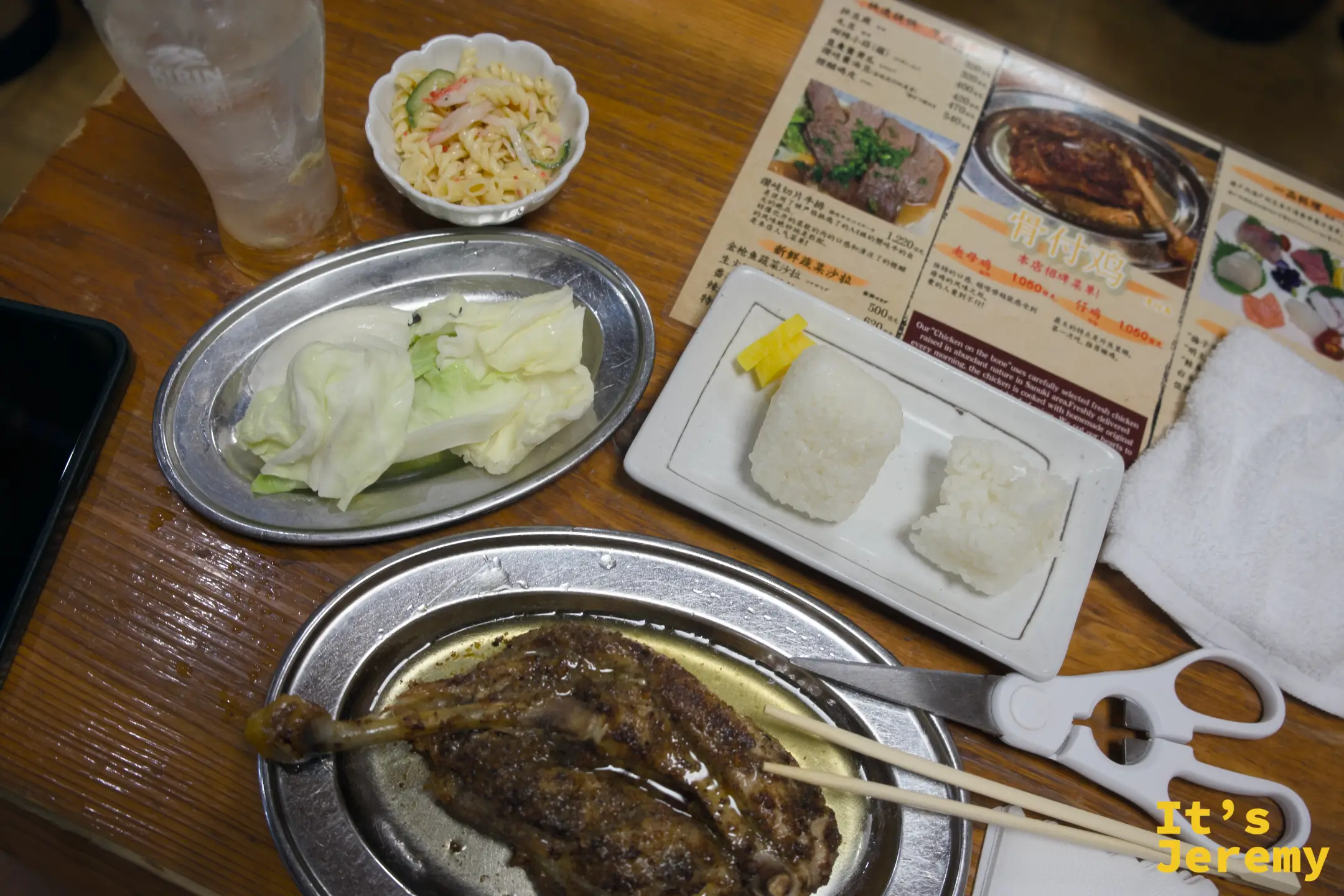 整桌展開：帶骨雞腿在不鏽鋼圓盤上，旁邊是高麗菜、小菜沙拉、塩むすび和剪刀