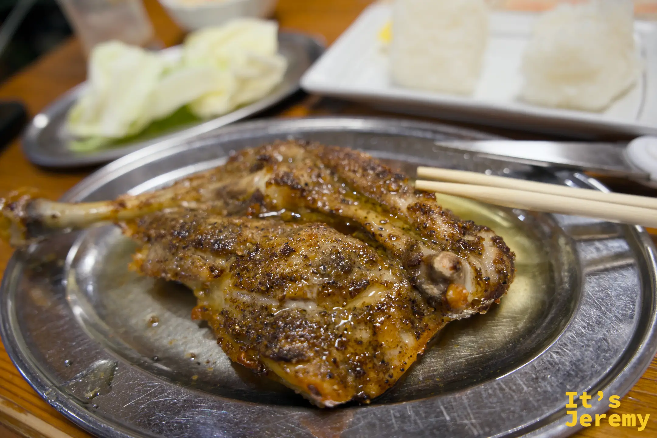 仔雞骨付鳥近景，香料脆皮在金屬圓盤上，筷子靠在側邊