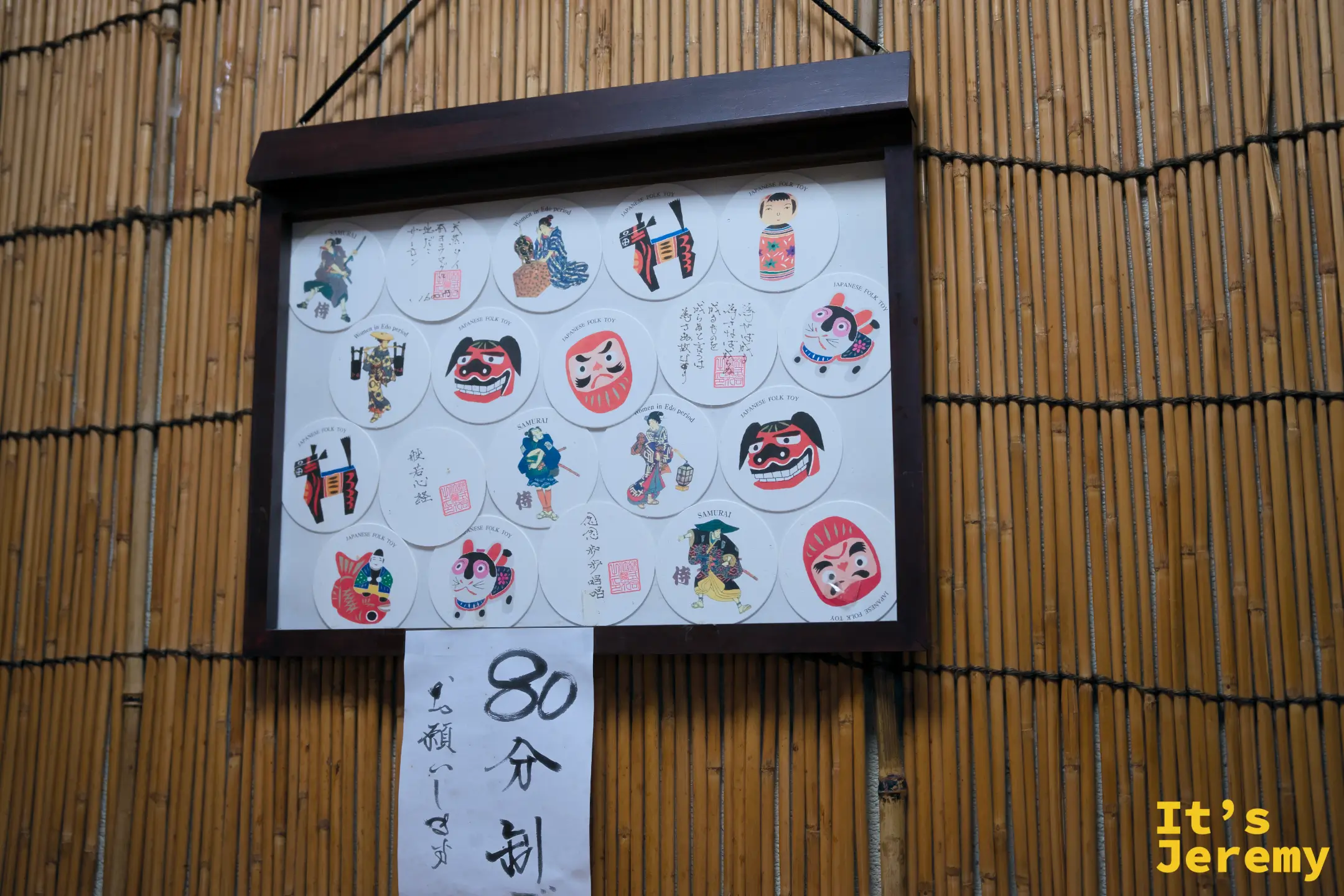 蘭丸店內牆面，竹簾背景上掛著一框日本插圖杯墊收藏，下方標示用餐限時 80 分鐘