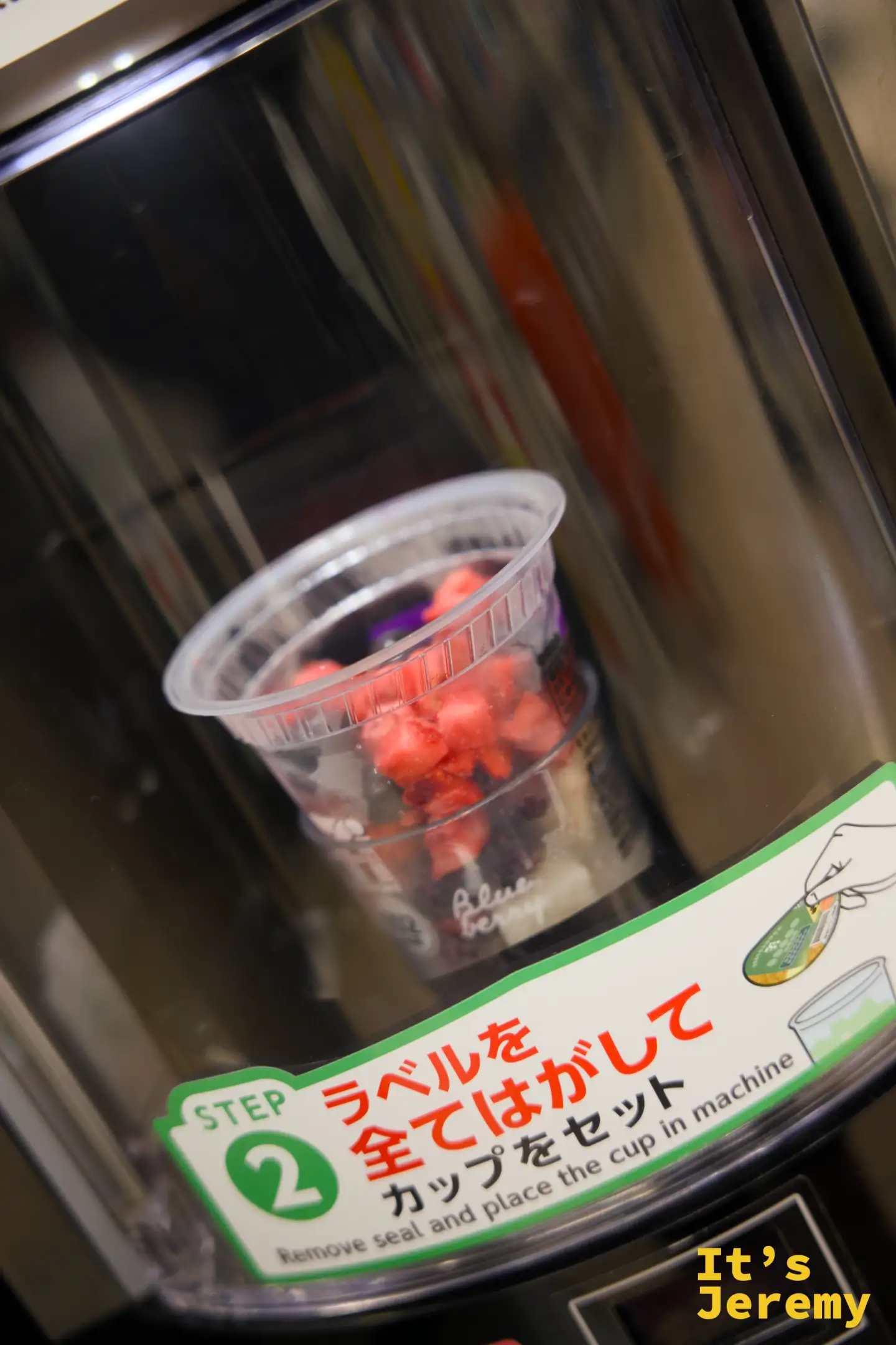 7-11 現打果汁機製作中的草莓莓果奶昔，透明杯中可見鮮紅草莓顆粒，旁邊有綠色操作說明貼紙