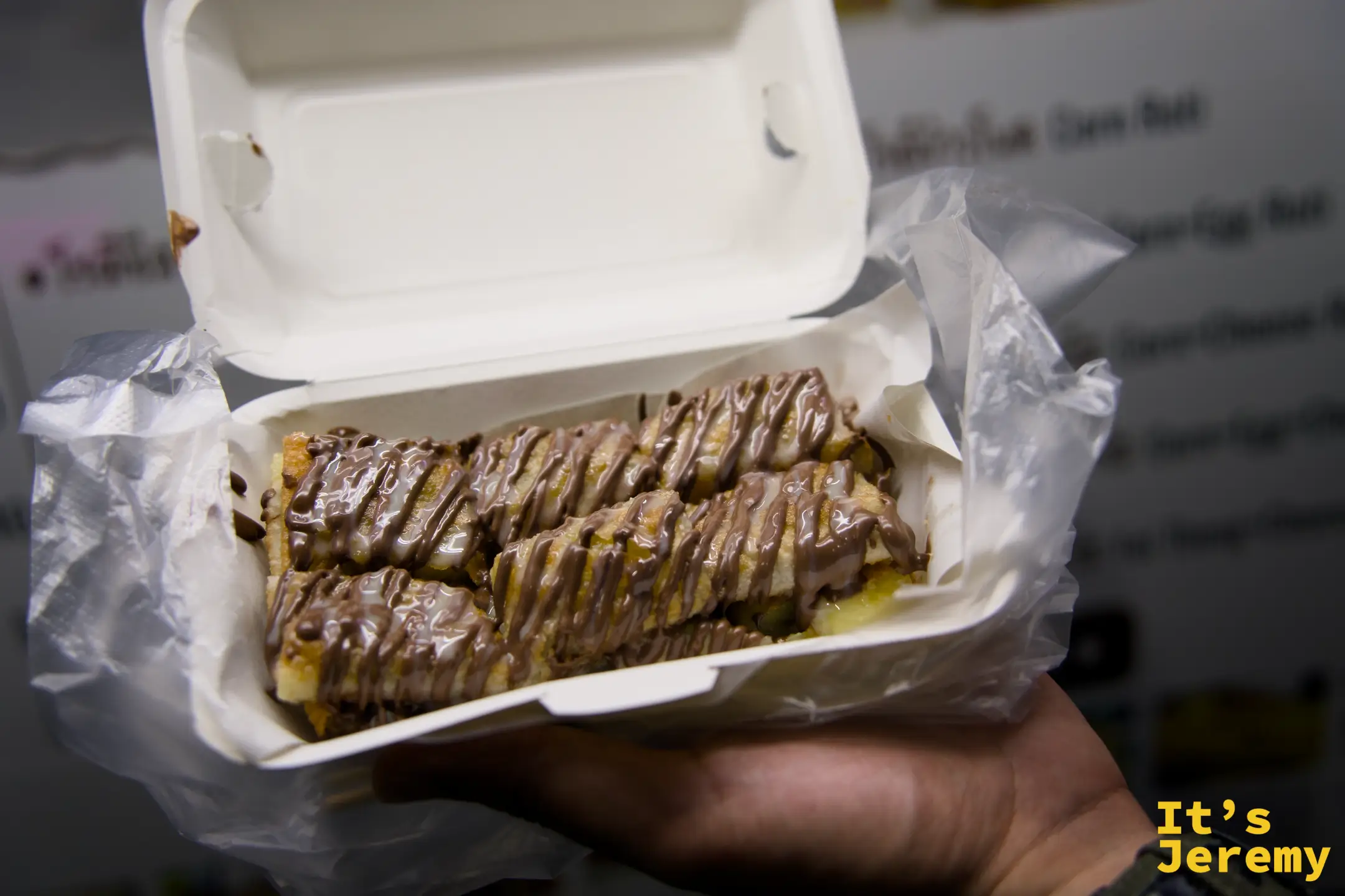 剛出爐的 Banana Nutella Roti，榛果巧克力醬淋在酥脆薄餅上，裝在外帶盒裡，油光反映燈光