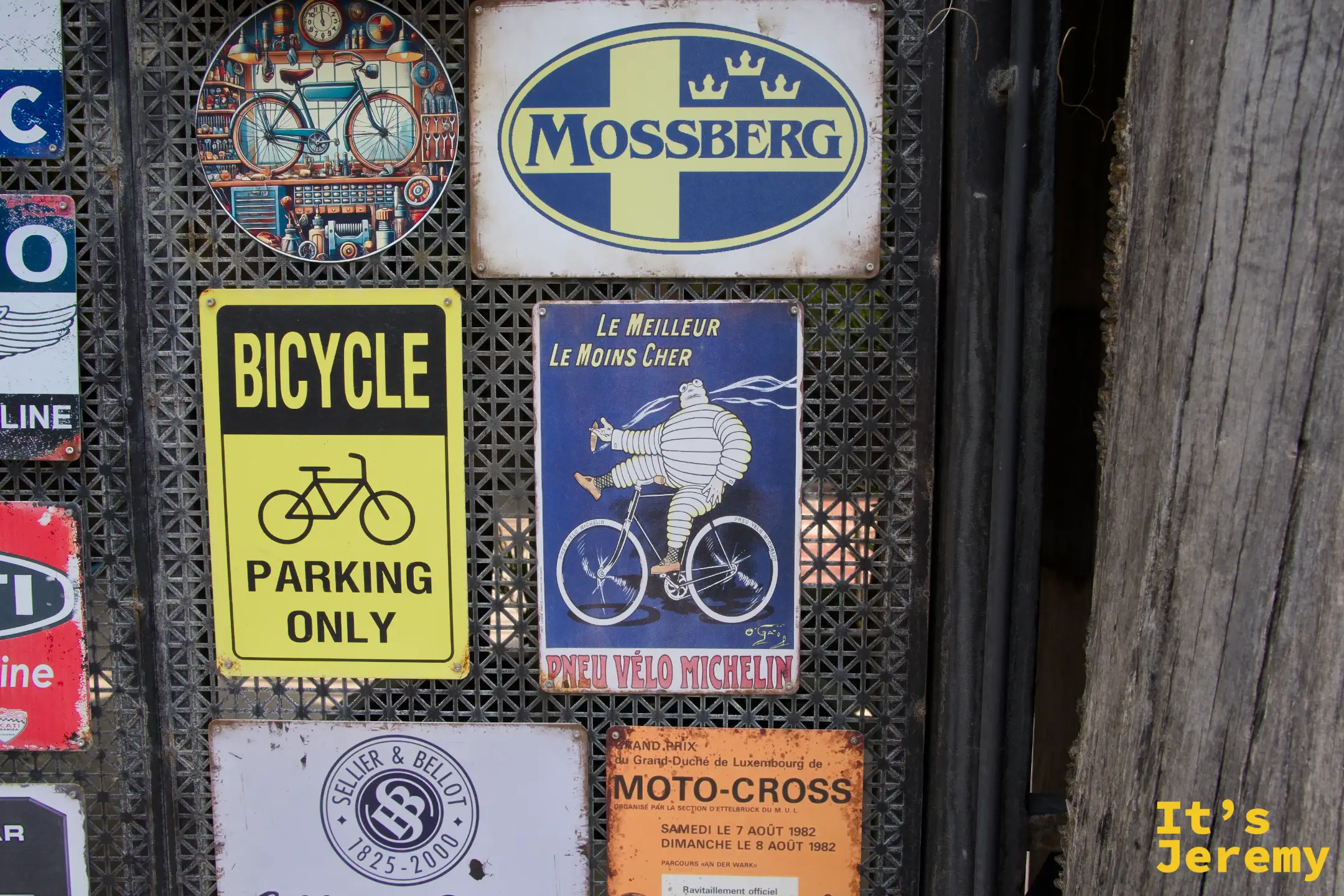 黃色 BICYCLE PARKING ONLY 告示牌旁，另一張藍底米其林寶寶騎車老鐵牌釘在格網上