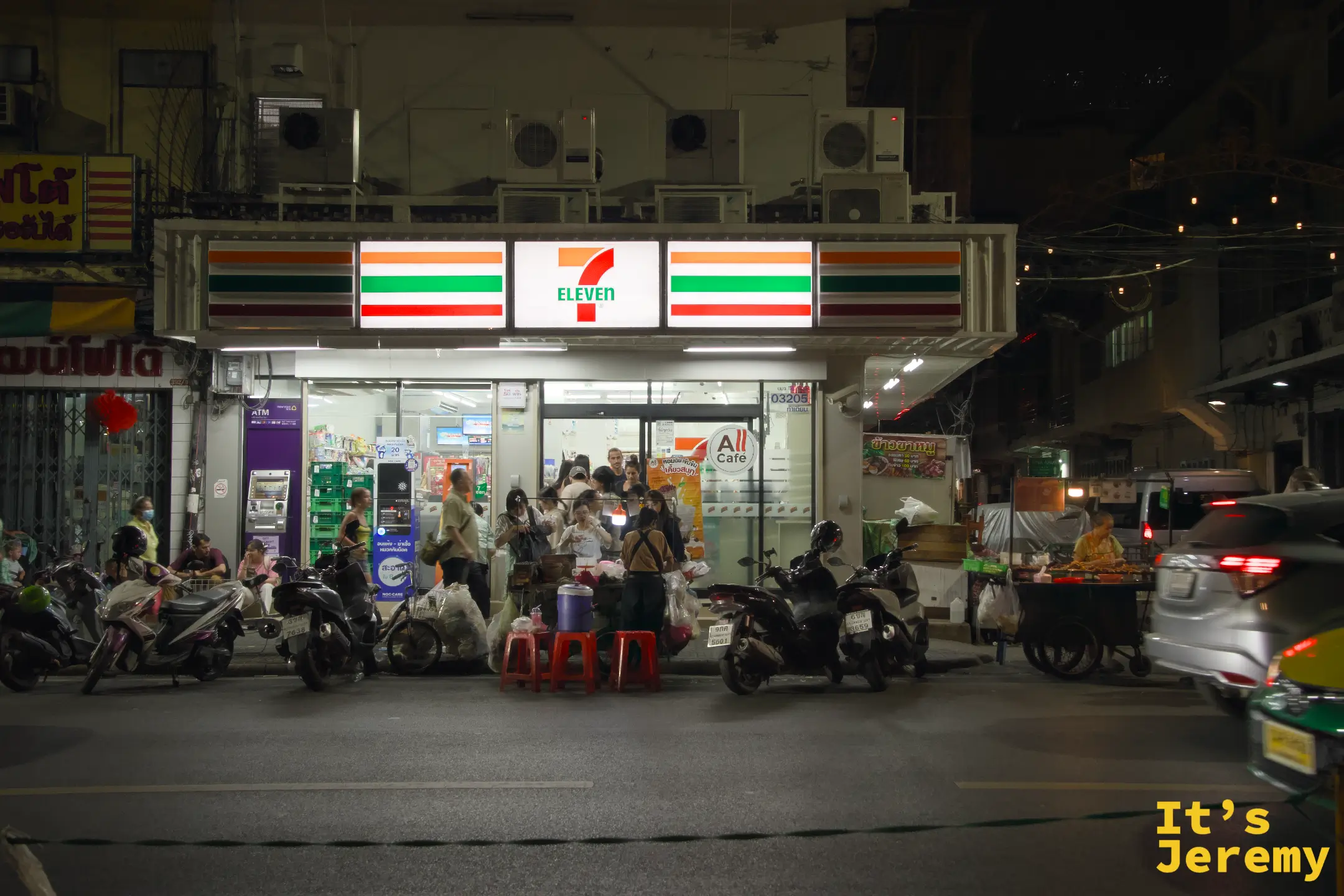 夜晚的 Tha Tien 7-Eleven，紅綠燈條把人行道切成兩半，門口擺著紅色塑膠凳的臨時小販