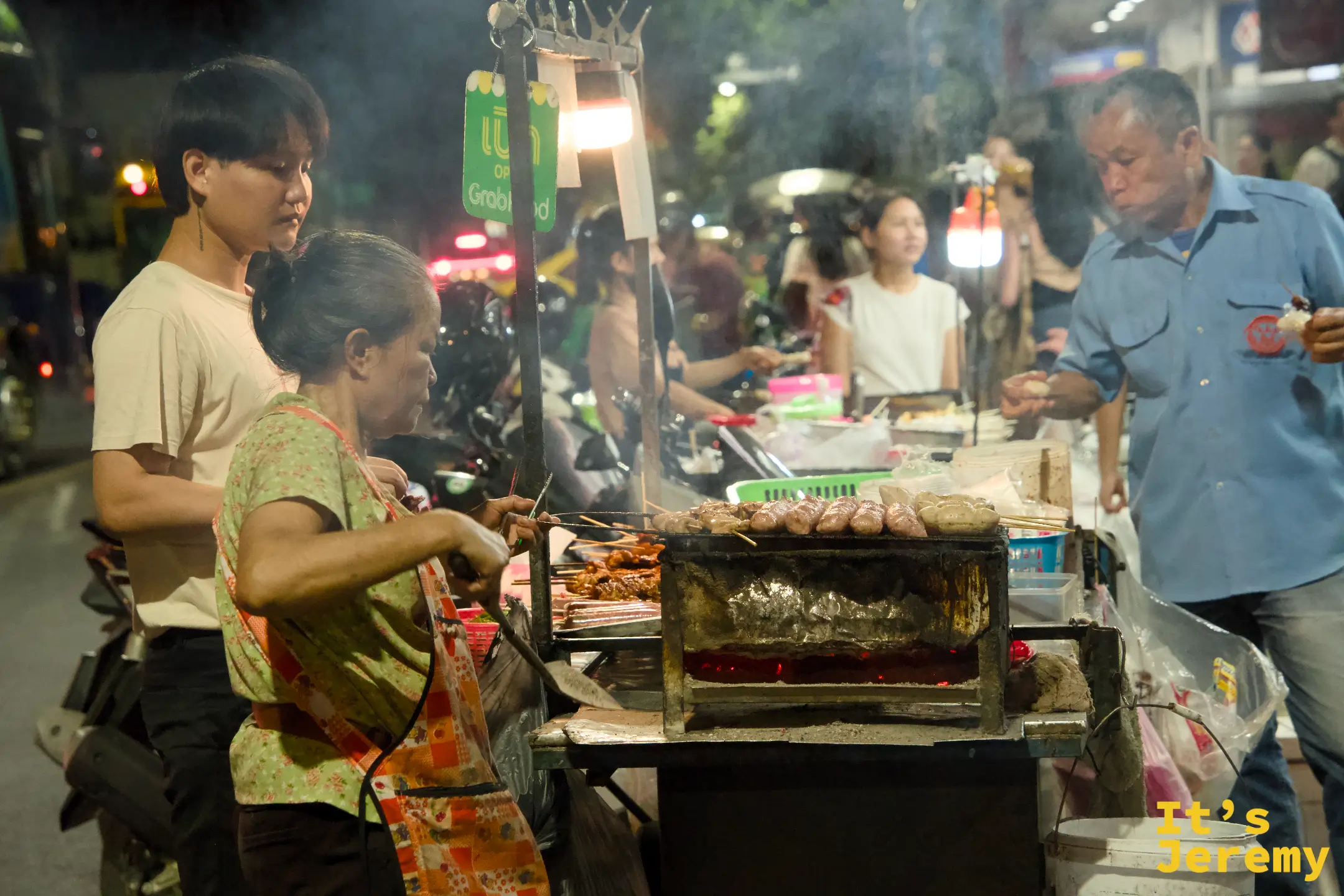 Tha Tien 街邊的炭烤老攤夜景，Grab Food 綠色招牌掛在頭頂上，傳統與外送平台的並存