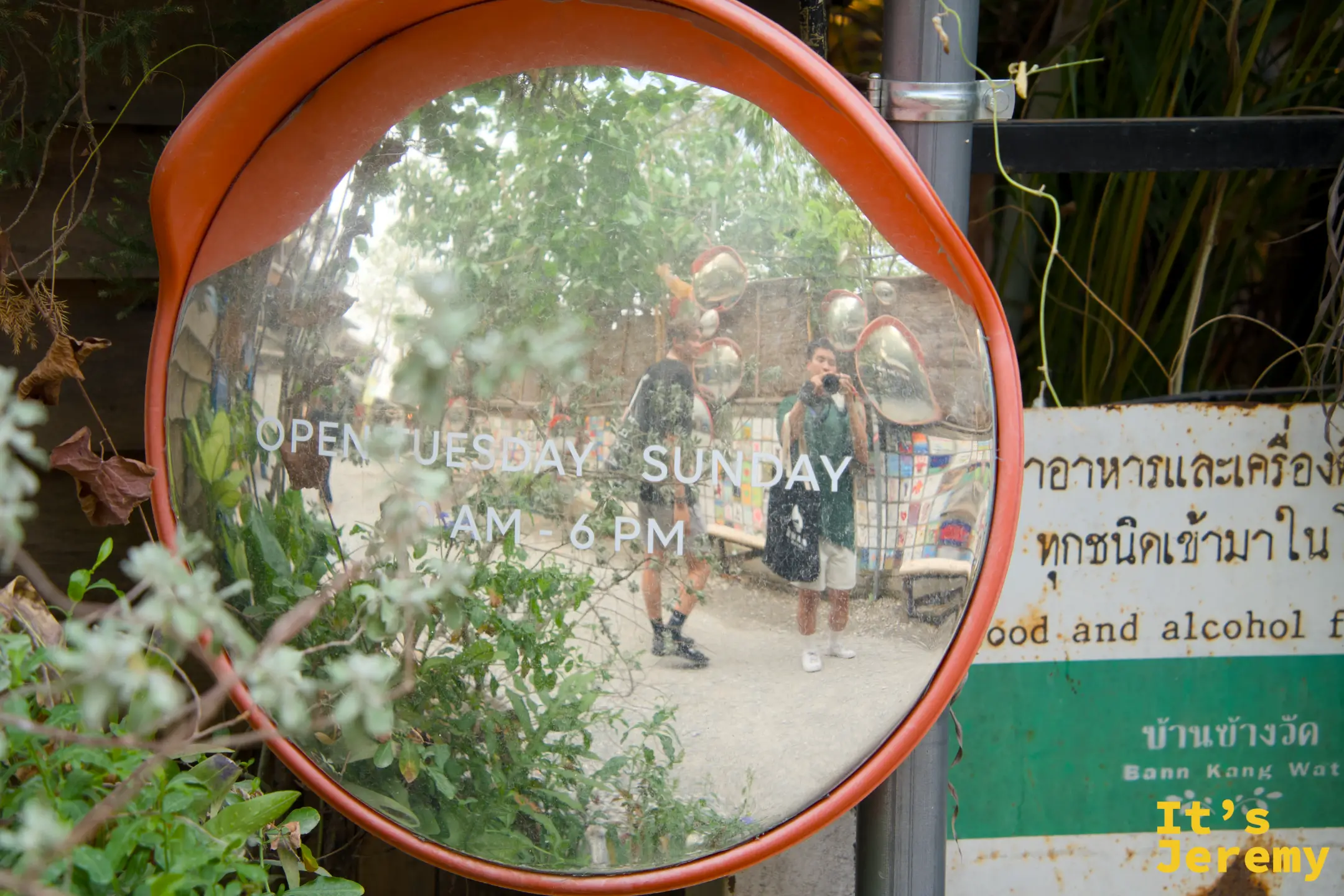 凸面鏡特寫，鏡面上寫著「OPEN TUESDAY SUNDAY AM-6PM」，旁邊綠色看板寫著「บ้านข้างวัด Baan Kang Wat」