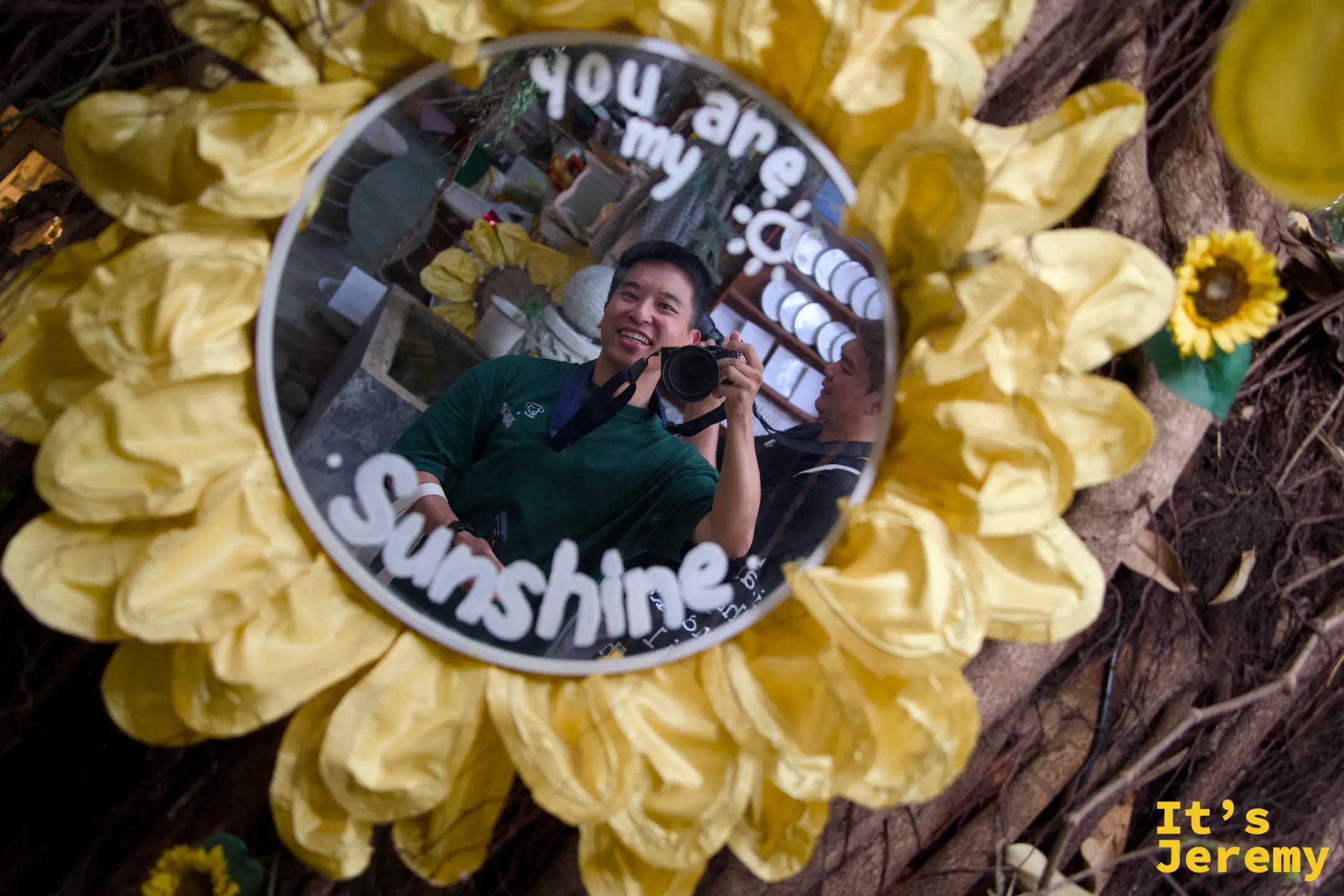 向日葵花框圓鏡俯拍，鏡面寫著「you are my sunshine」，鏡中倒映著拿相機的笑著的訪客