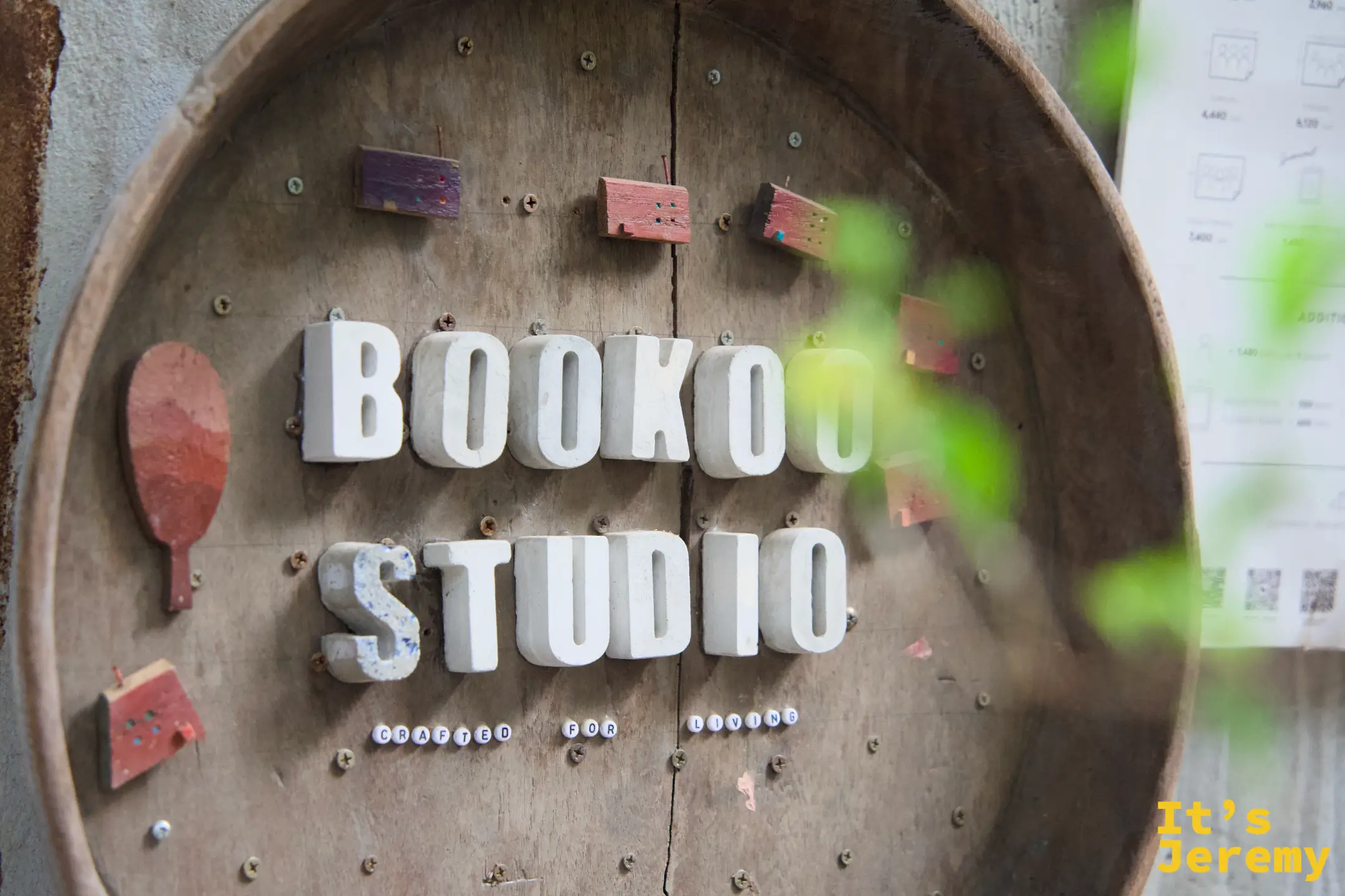 BOOKOO STUDIO 木製圓形招牌近拍，立體白字嵌在舊木桶上，旁邊有小塊彩色木片裝飾