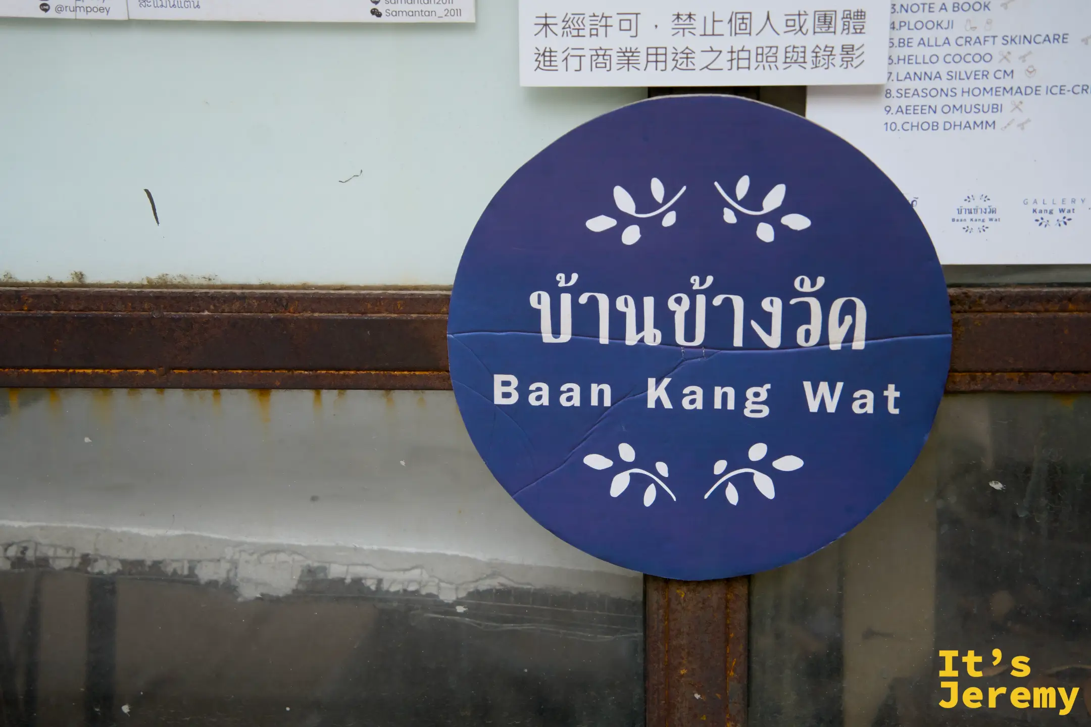 Baan Kang Wat 藍紫色圓形招牌，旁邊牆上有各商店清單與中文禁止商業拍攝告示