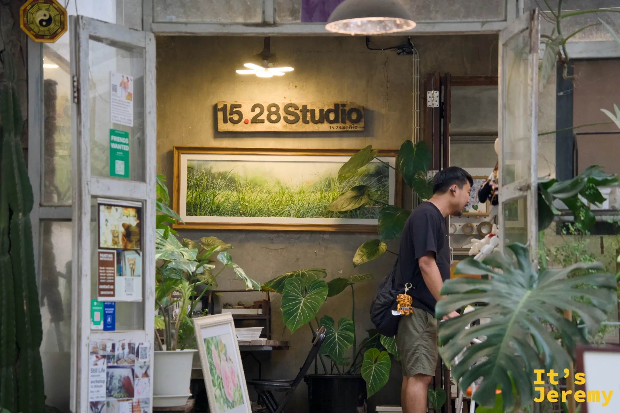 15.28 Studio 店鋪玻璃門內，牆上掛著大幅稻田風景畫，燈光溫暖，一位男生在門口瀏覽
