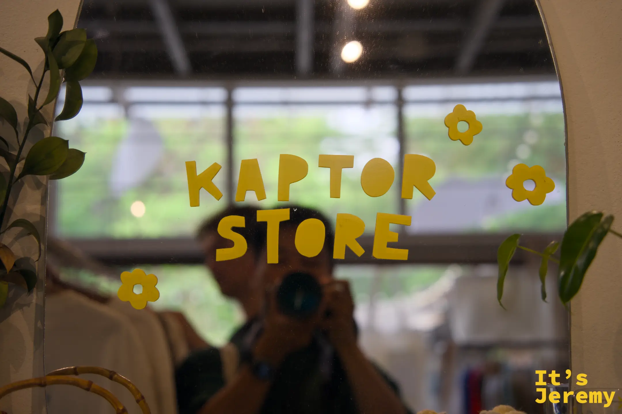 Kaptor Store 鏡子，橘色字母「KAPTOR STORE」貼在拱形鏡面上，搭配小花朵圖案，鏡中倒映著攝影者