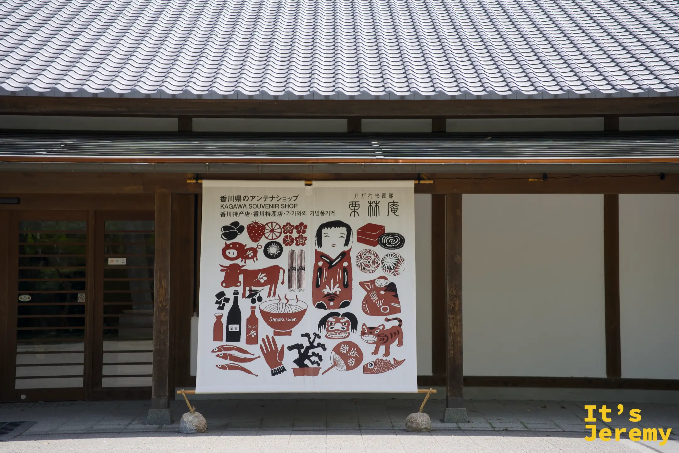 東林庵外牆掛著的大型插畫布幔，紅黑兩色描繪香川縣的代表元素：烏龍麵、橄欖、鯛魚、魔女宅急便等