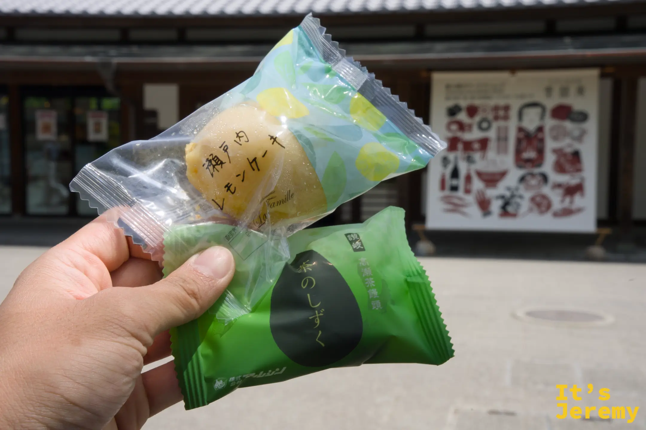 一隻手拿著兩種真空包裝的香川縣小點心：上方是「瀬戸内レモンケーキ」，下方是綠色的「讚岐 茶のしずく」，背景是東林庵的外牆