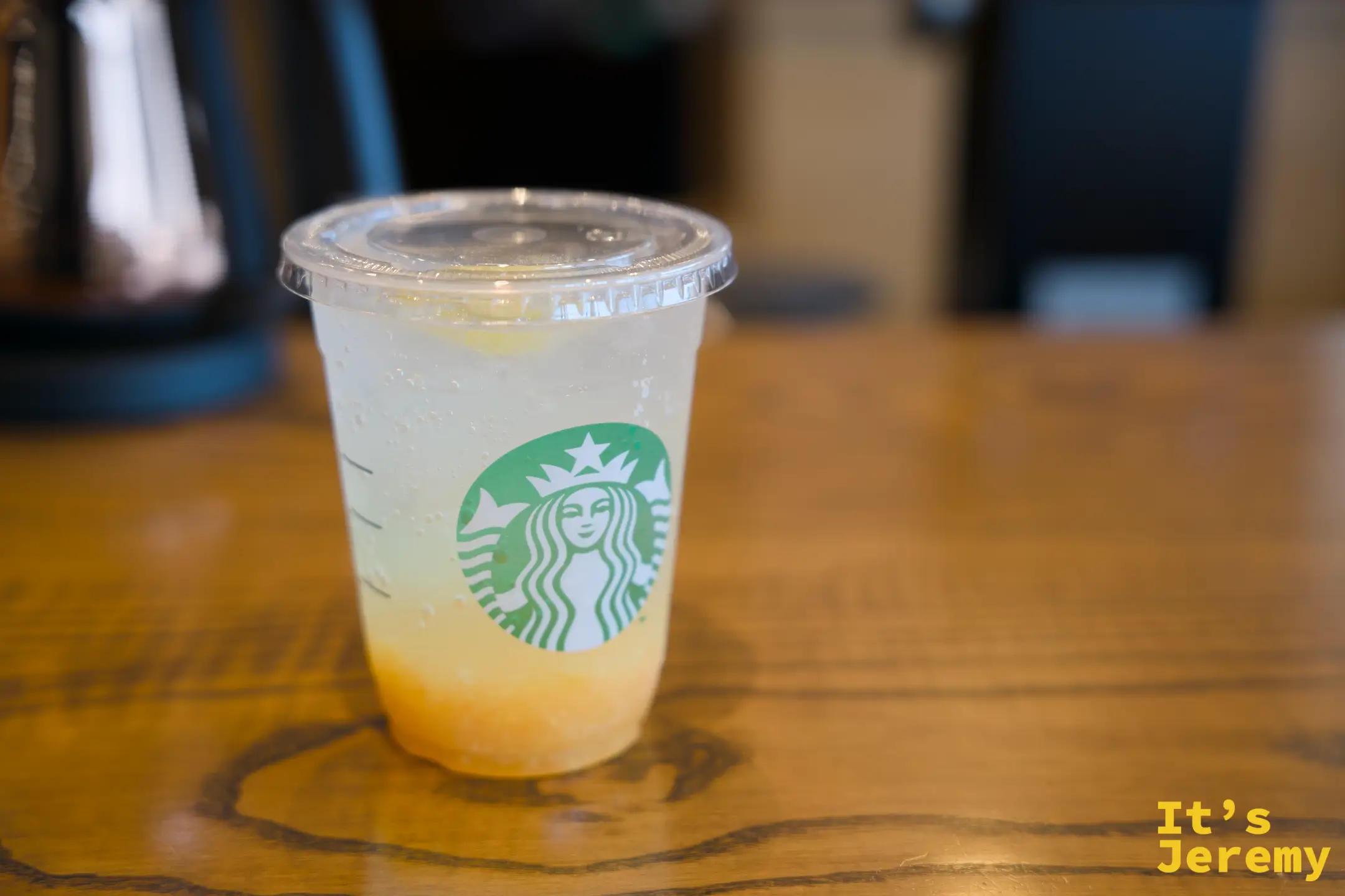 星巴克透明杯裝柚子蘇打，淡黃色飲料底部帶橙，置於木質桌面上