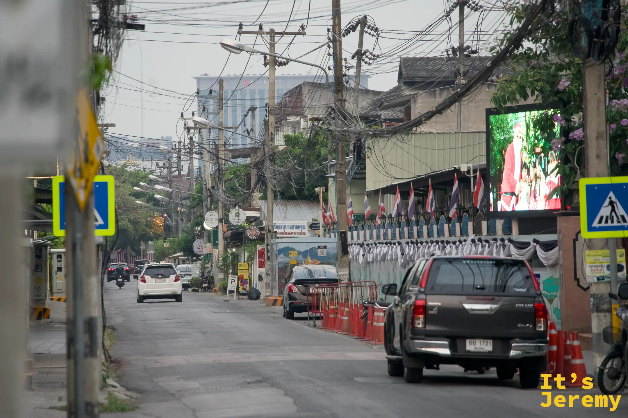 掛著一排泰國國旗的街道，深色皮卡車停在橘色三角錐旁