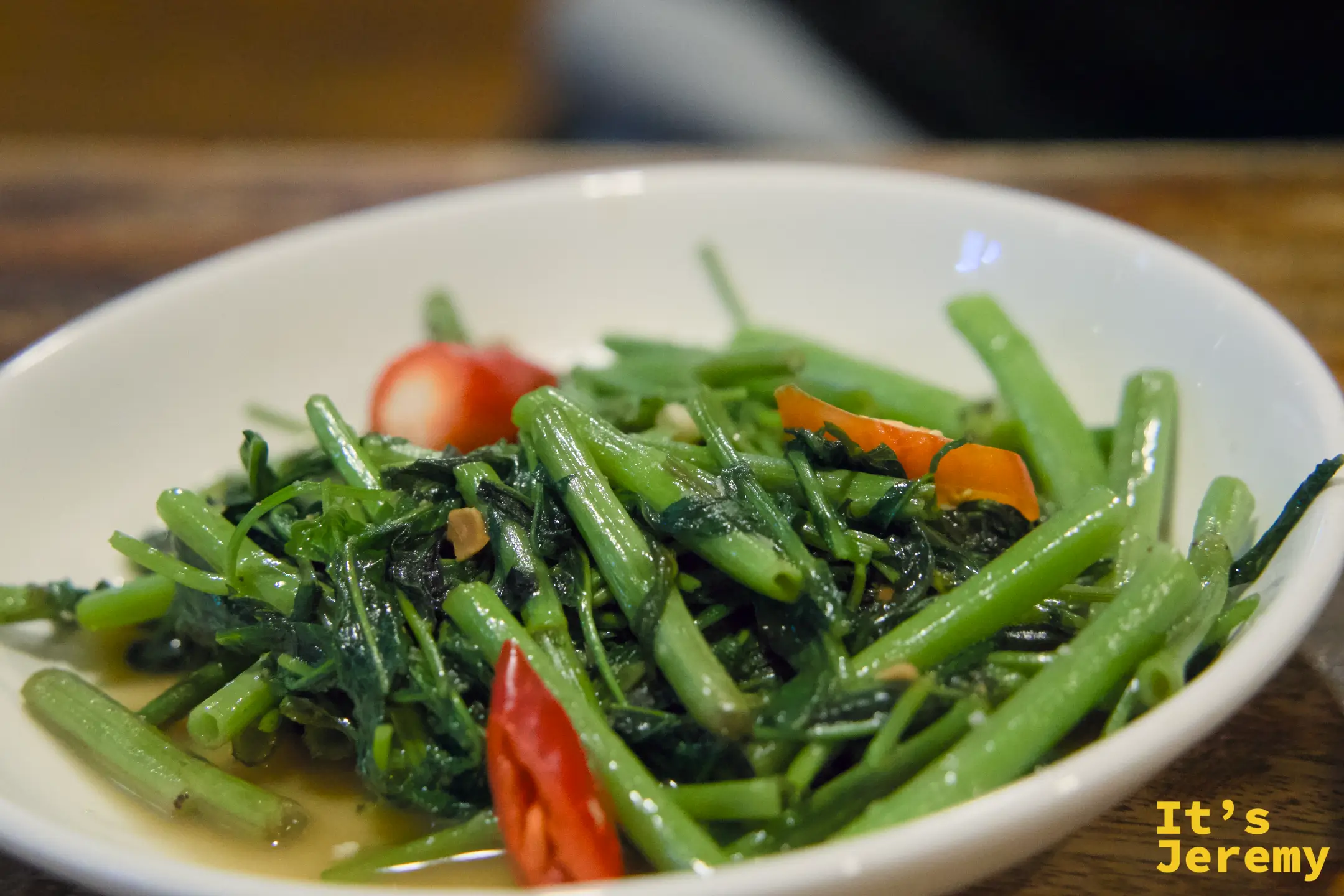 ผัดผักบุ้ง 炒空心菜，翠綠空心菜配上紅辣椒，底部有淡色醬汁