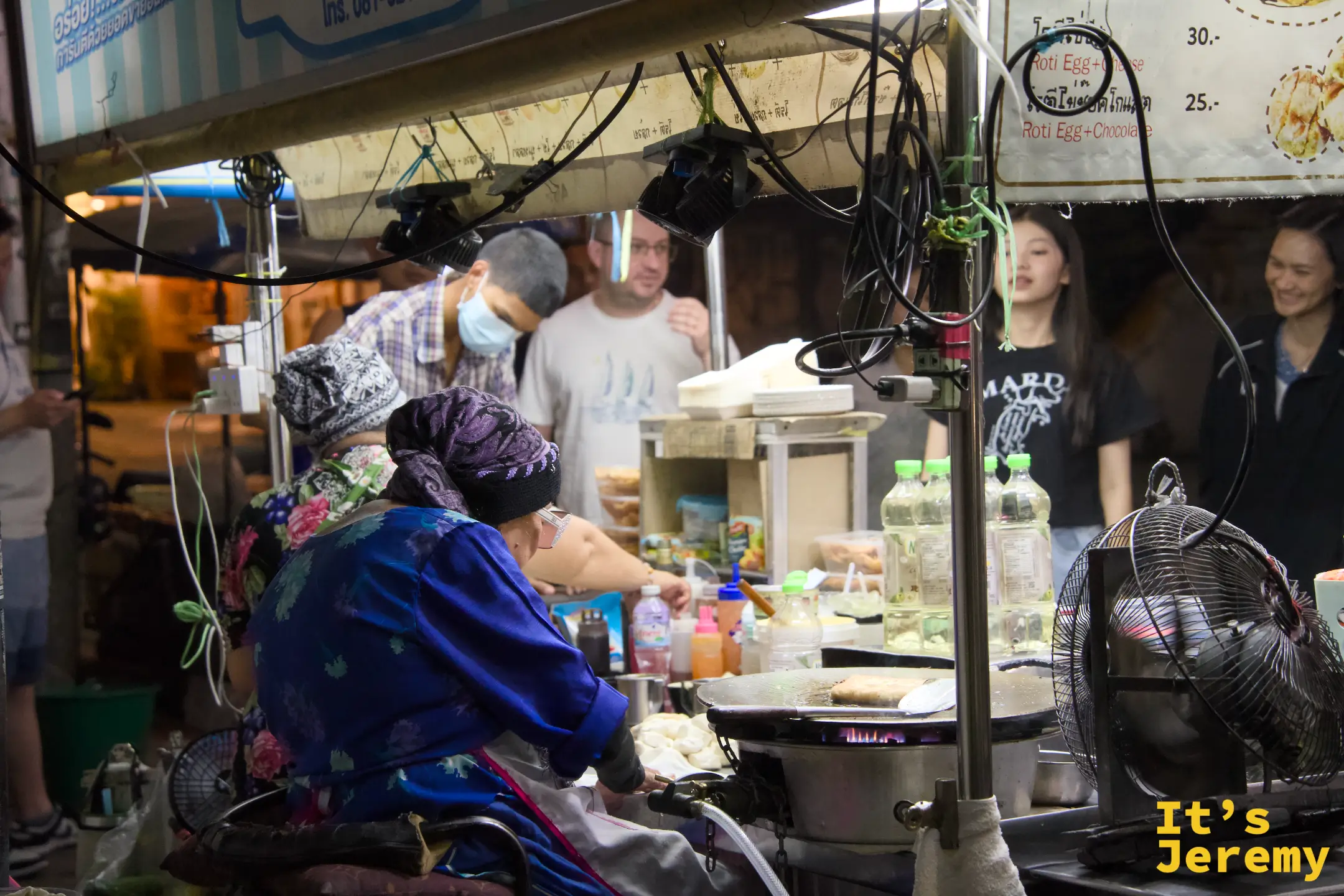 攤位側面視角：奶奶坐在鐵板前工作，攤外圍著等餐與拍照的客人