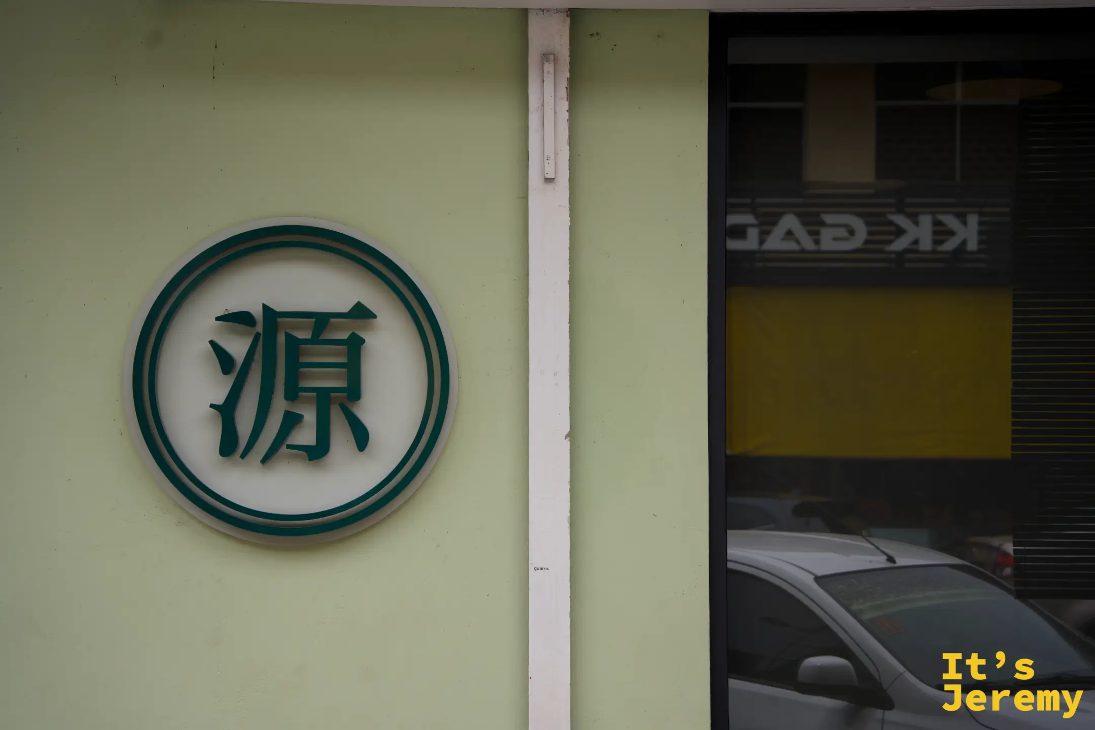 建築側牆上的圓形「源」品牌標誌，淺黃綠色牆面搭配深綠色字體