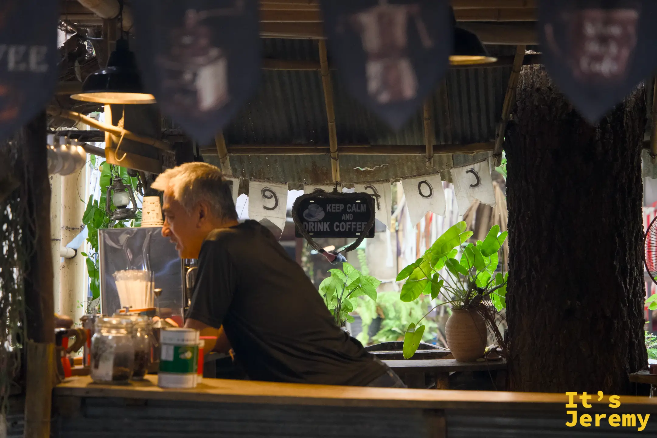 咖啡攤的大叔在攤位裡備料，頭頂掛著「KEEP CALM AND DRINK COFFEE」的牌子