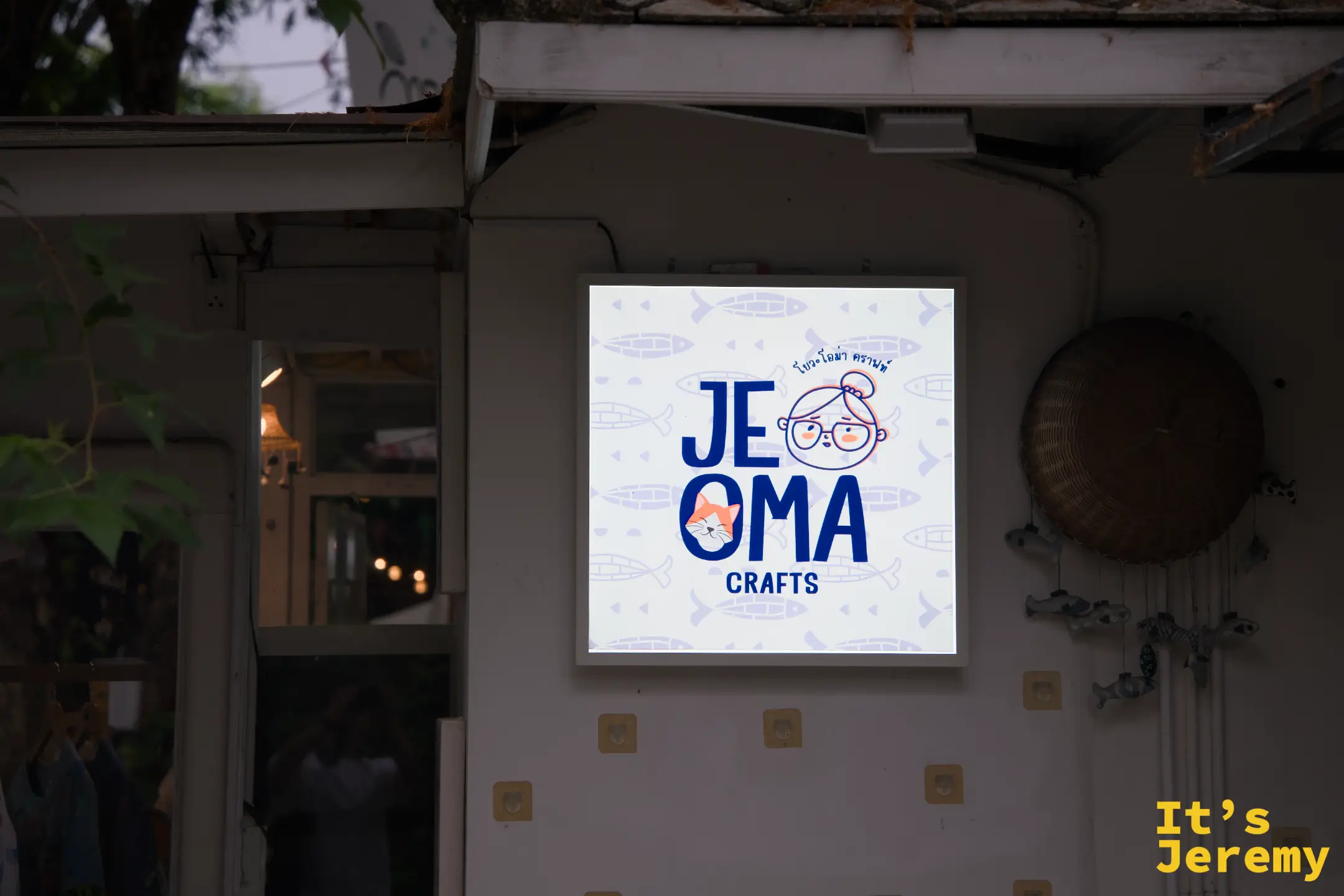 JE OMA CRAFTS 的方形燈箱招牌，藍色字體配戴眼鏡奶奶與貓咪的插畫 logo
