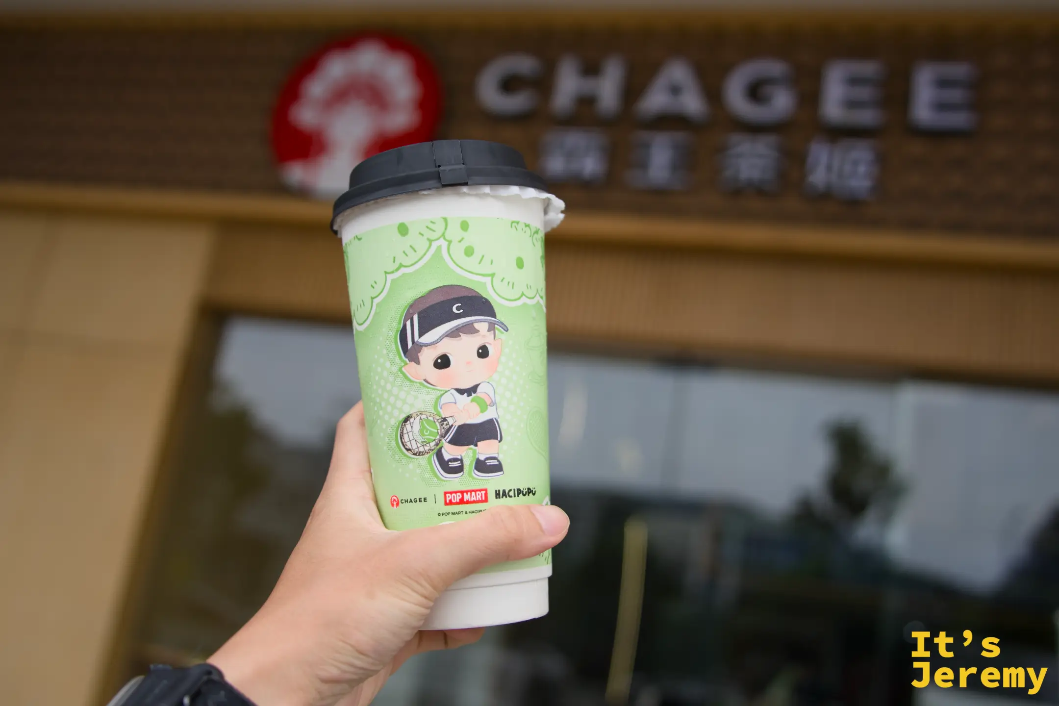手持 CHAGEE × POP MART HACIPUPU 聯名款綠色飲料杯，背景是 CHAGEE 門市招牌