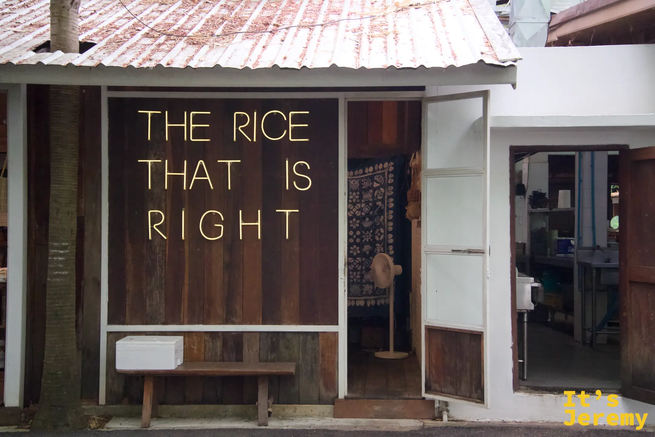 木牆上的黃色霓虹燈字「THE RICE THAT IS RIGHT」，旁邊門內掛著藍染布簾