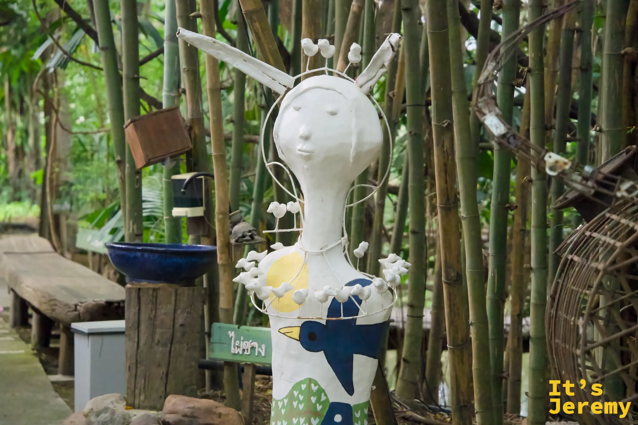 竹林旁的白色人形雕塑，長耳造型、身上畫著藍色小鳥圖案，掛著白色串珠項圈