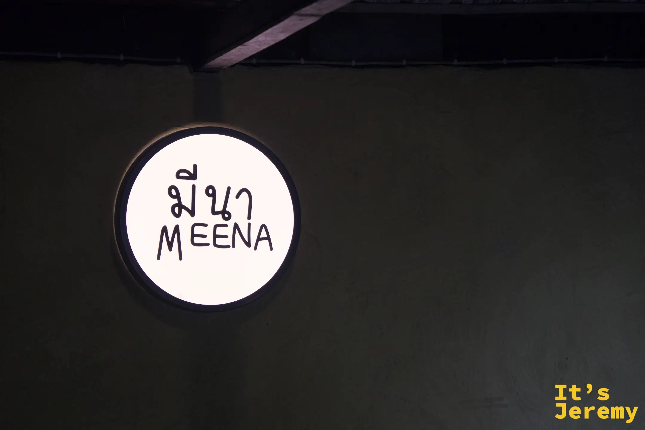 Meena 的圓形燈箱招牌，白底寫著泰文 มีนา 與英文 MEENA