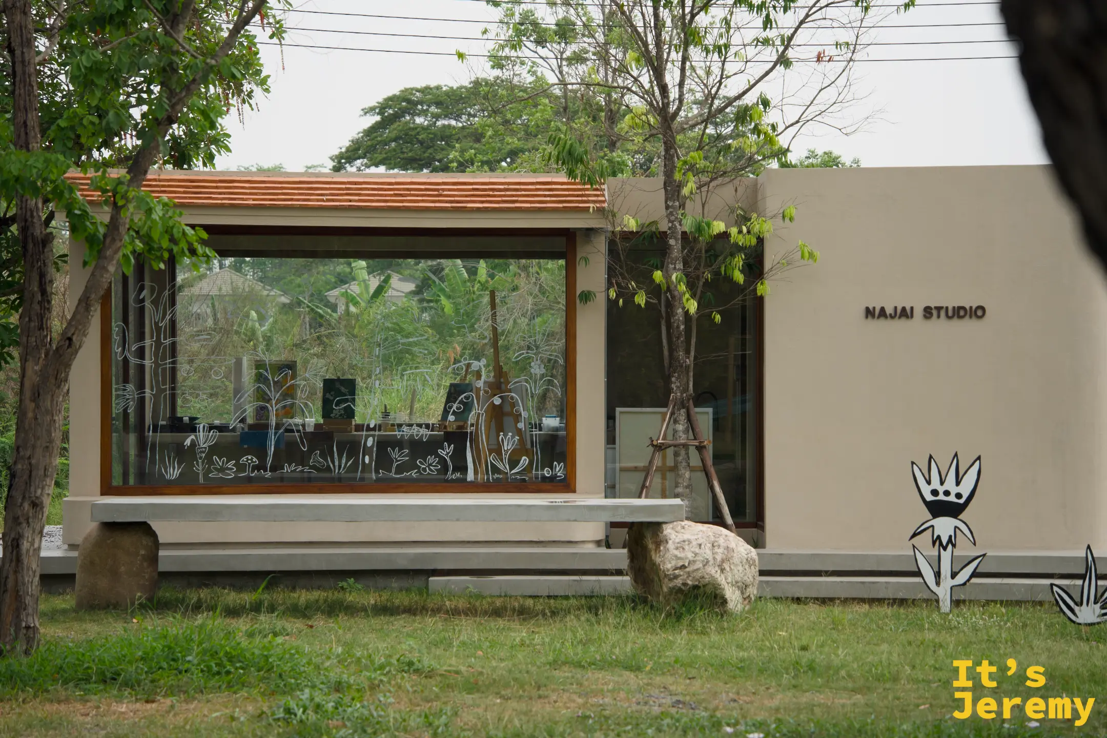 NAJAI STUDIO 的水泥建築外觀，大面落地窗上畫著插畫線條，門口立著黑白花朵剪板