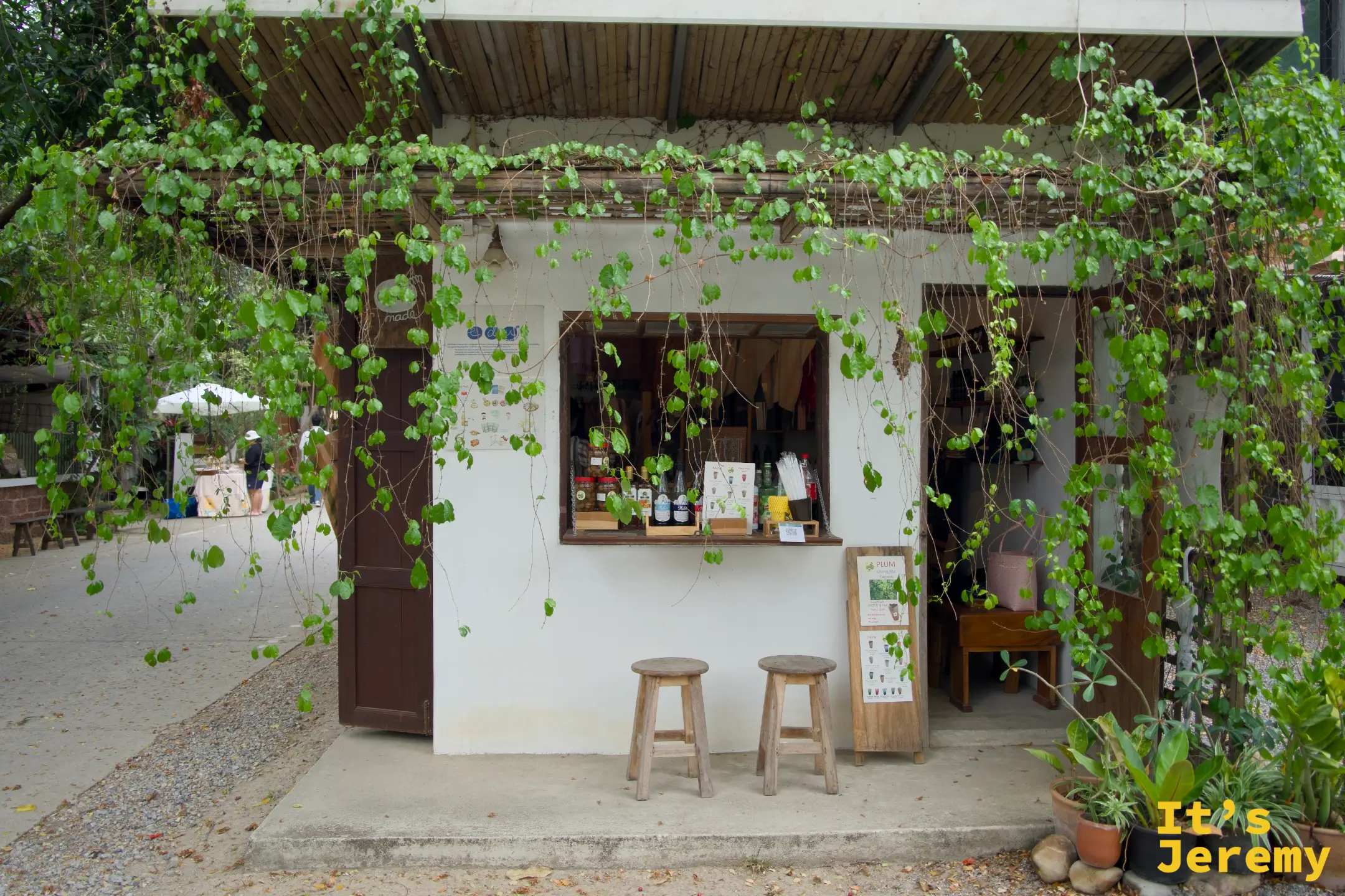 EDUMade 的白色小屋店面，藤蔓從棚架垂落成綠簾，點餐口前擺著兩張木凳
