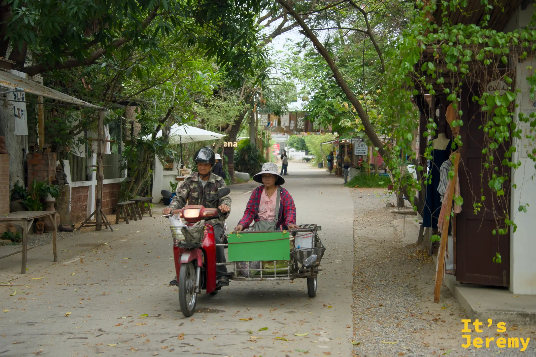 載貨三輪摩托車駛過市集主街，戴斗笠的攤販大姐坐在側斗裡