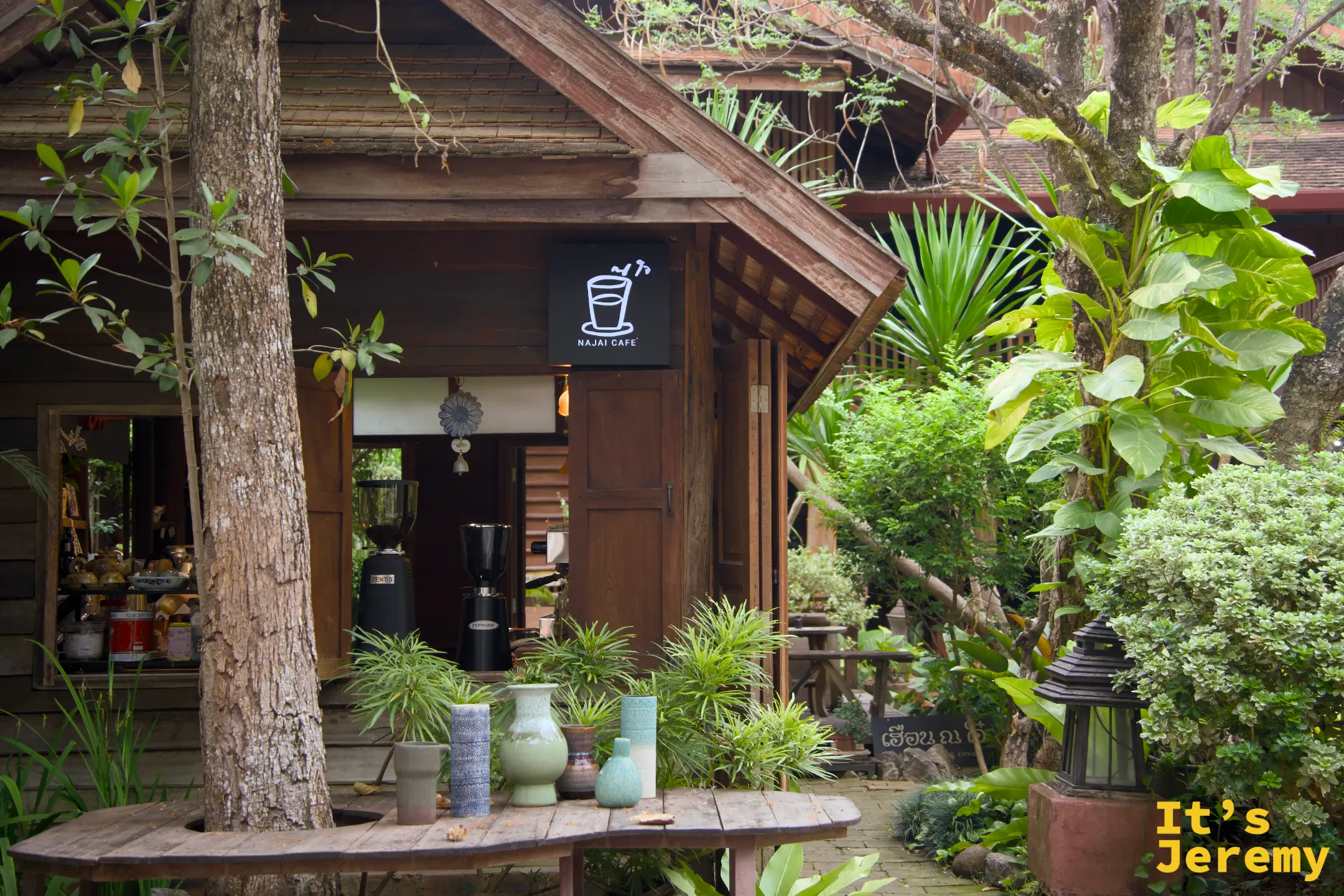 NAJAI CAFE 的老木屋店面，門口長桌上擺著綠色陶花瓶，被植物包圍