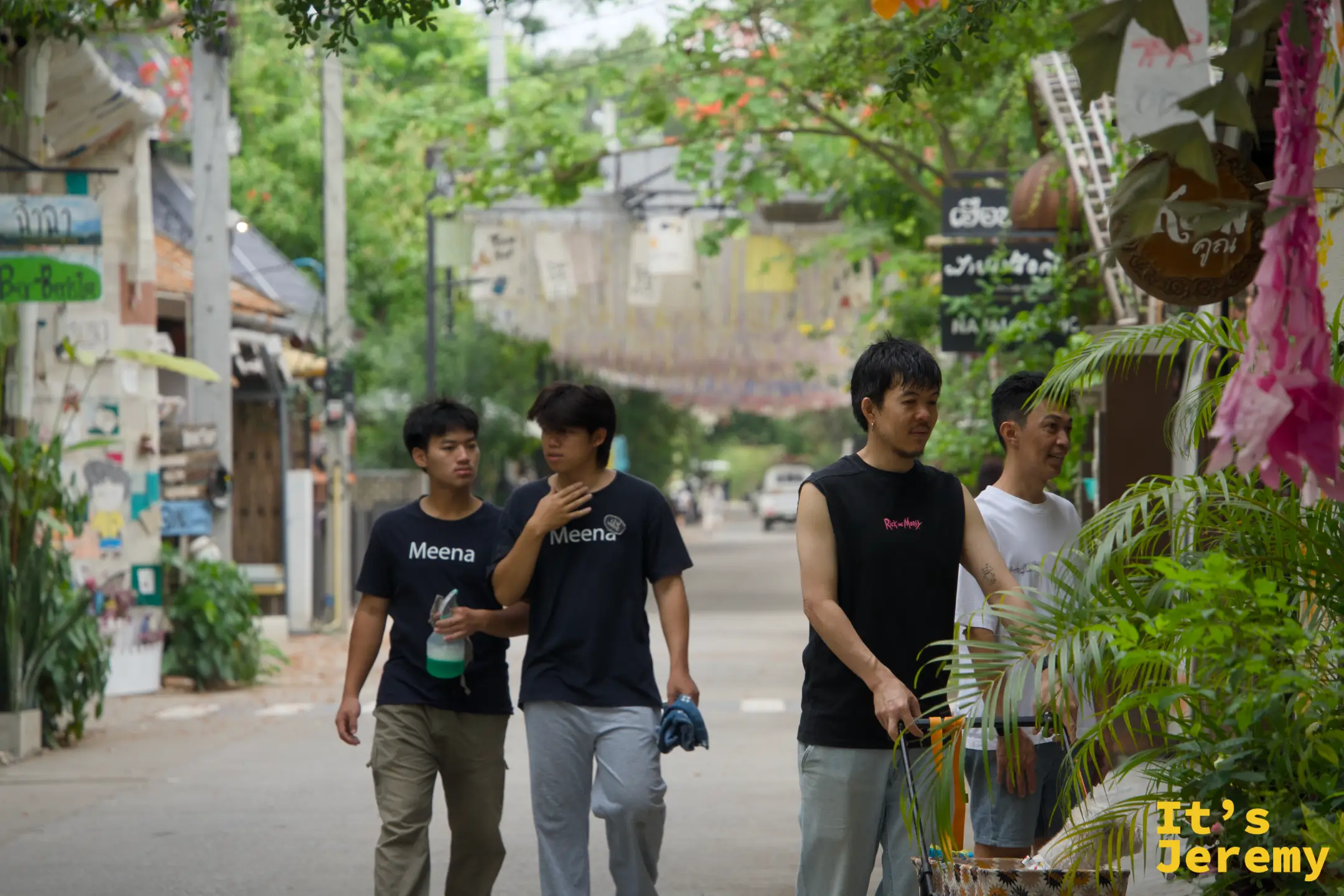 穿著 Meena 字樣 T 恤的店員們走在市集主街上，頭頂是布條天棚