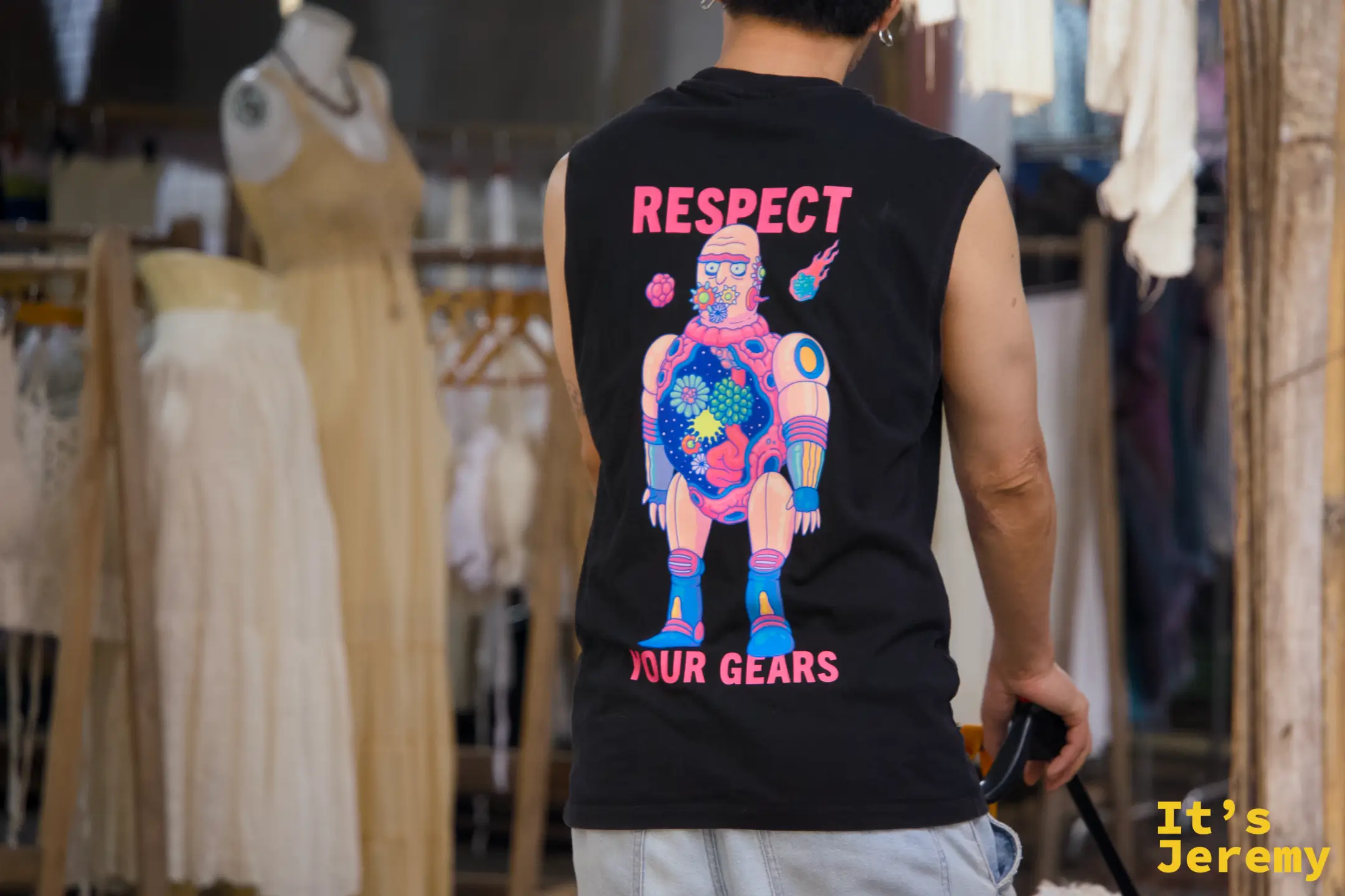穿著「RESPECT YOUR GEARS」插畫背心的男子背影，前方是掛滿棉麻洋裝的服飾攤