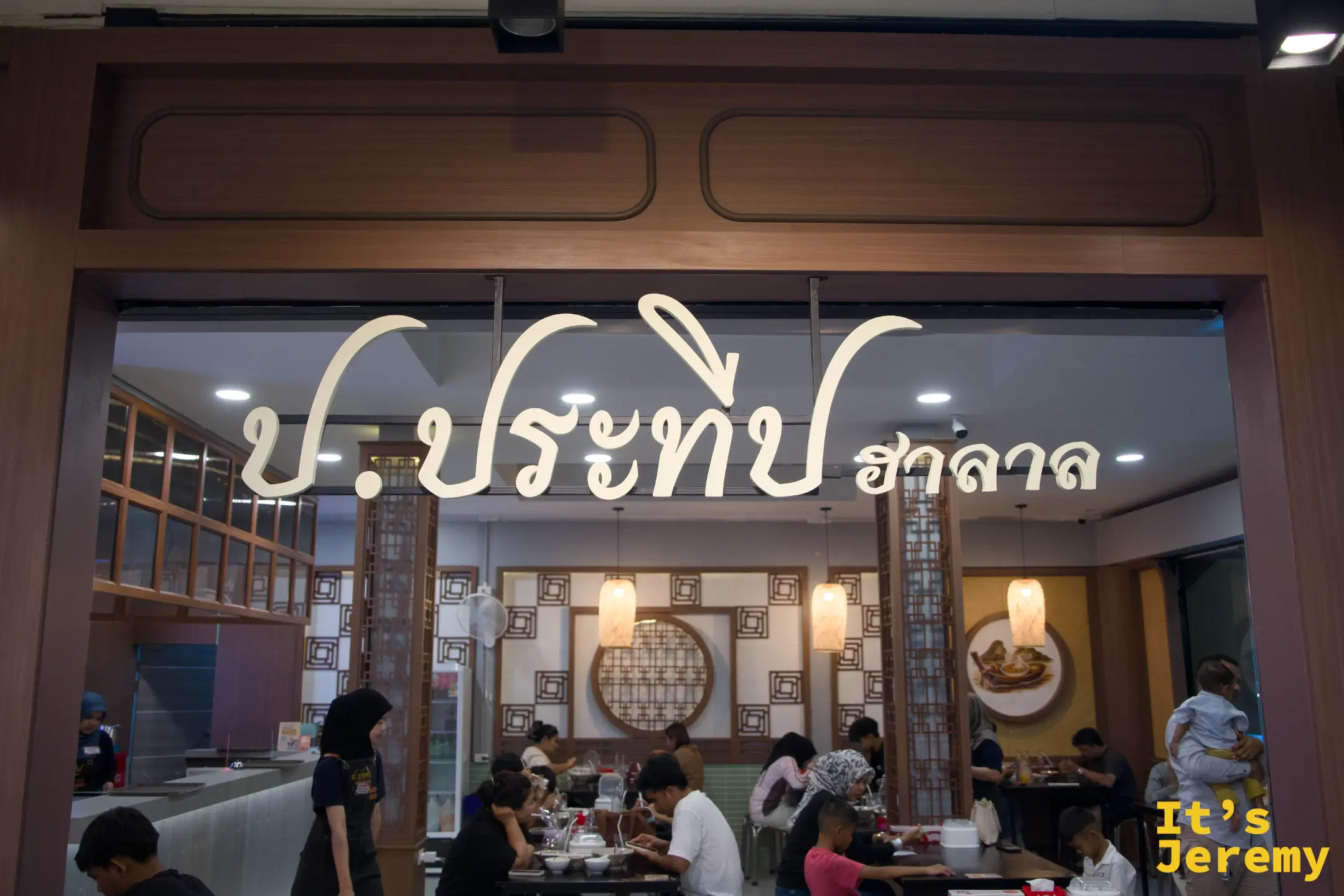 船麵店的米色立體泰文店招掛在挑高門面上，店內木質窗花裝潢，座位坐滿用餐的本地家庭