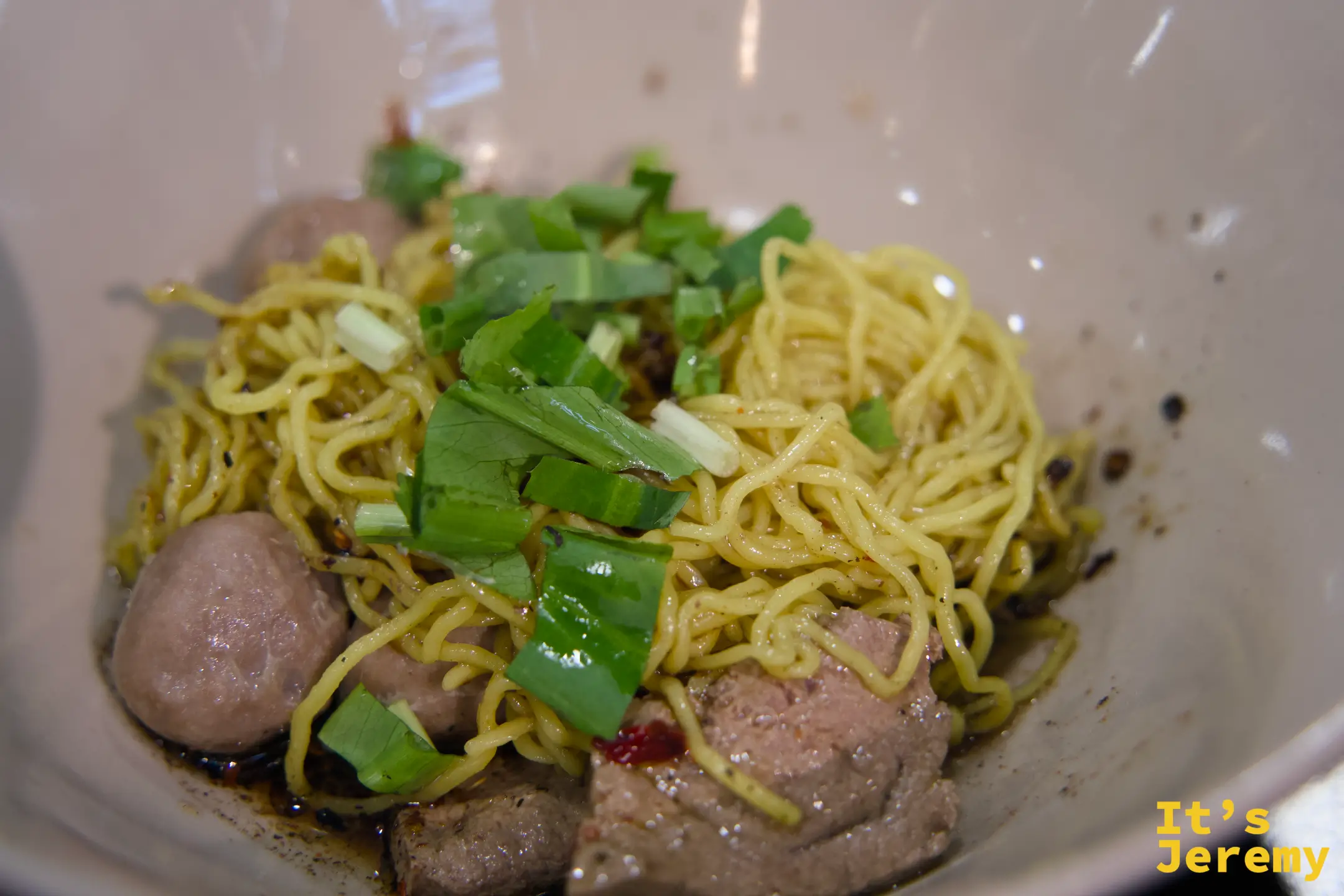 乾拌船麵的特寫，黃色雞蛋麵上鋪著燙牛肉片、牛肉丸與大把翠綠的青菜蔥段
