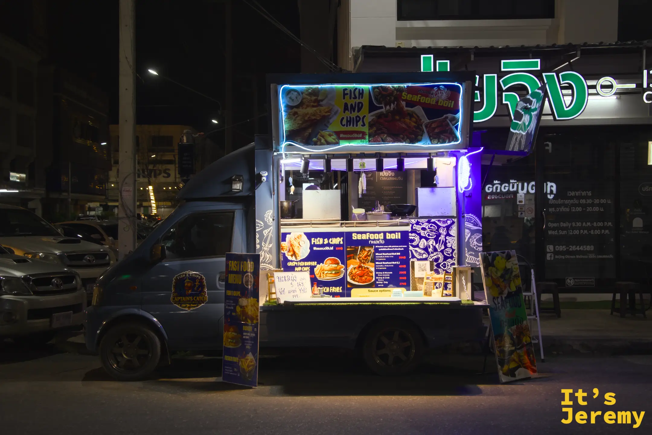 深藍色的炸魚薯條餐車亮著藍色霓虹燈，車身掛著 Fish and Chips 與 Seafood Boil 的菜單看板