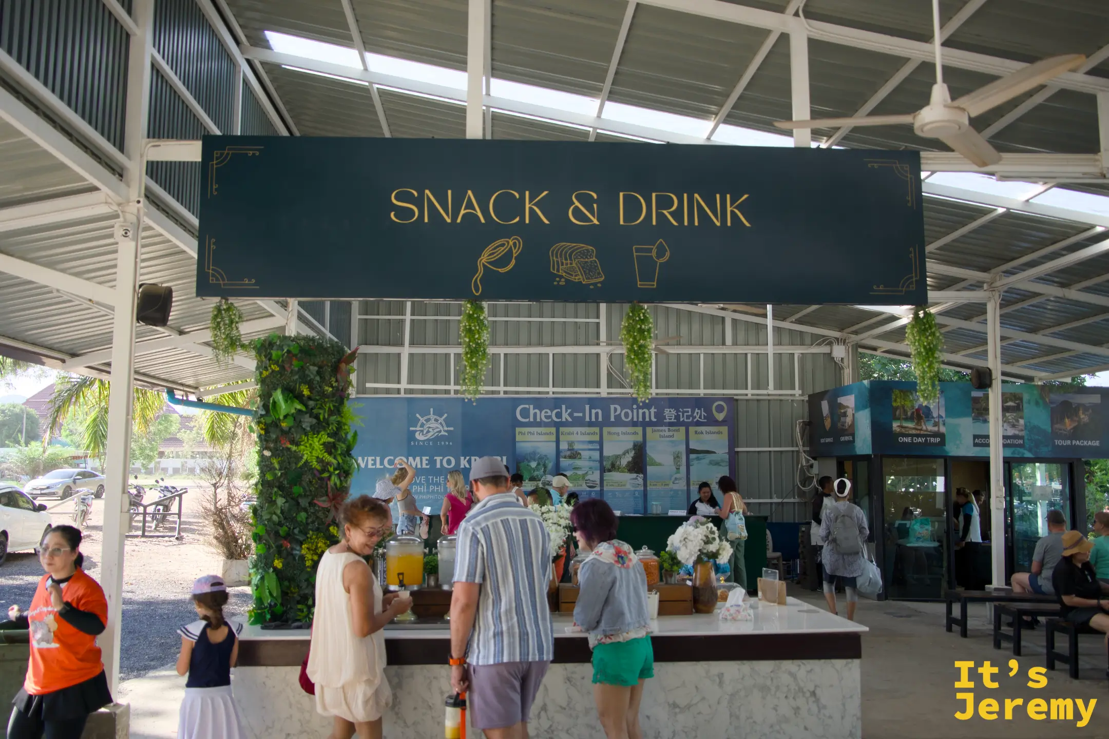 報到處的 Snack & Drink 吧台，旅客在取用飲料，後方有 Check-In Point 登記處