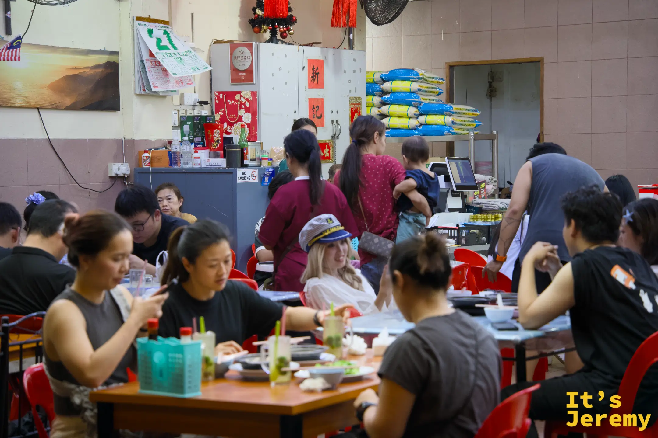 店內用餐場景，座位幾乎全滿，後方可見「新記」招牌與工作人員備餐