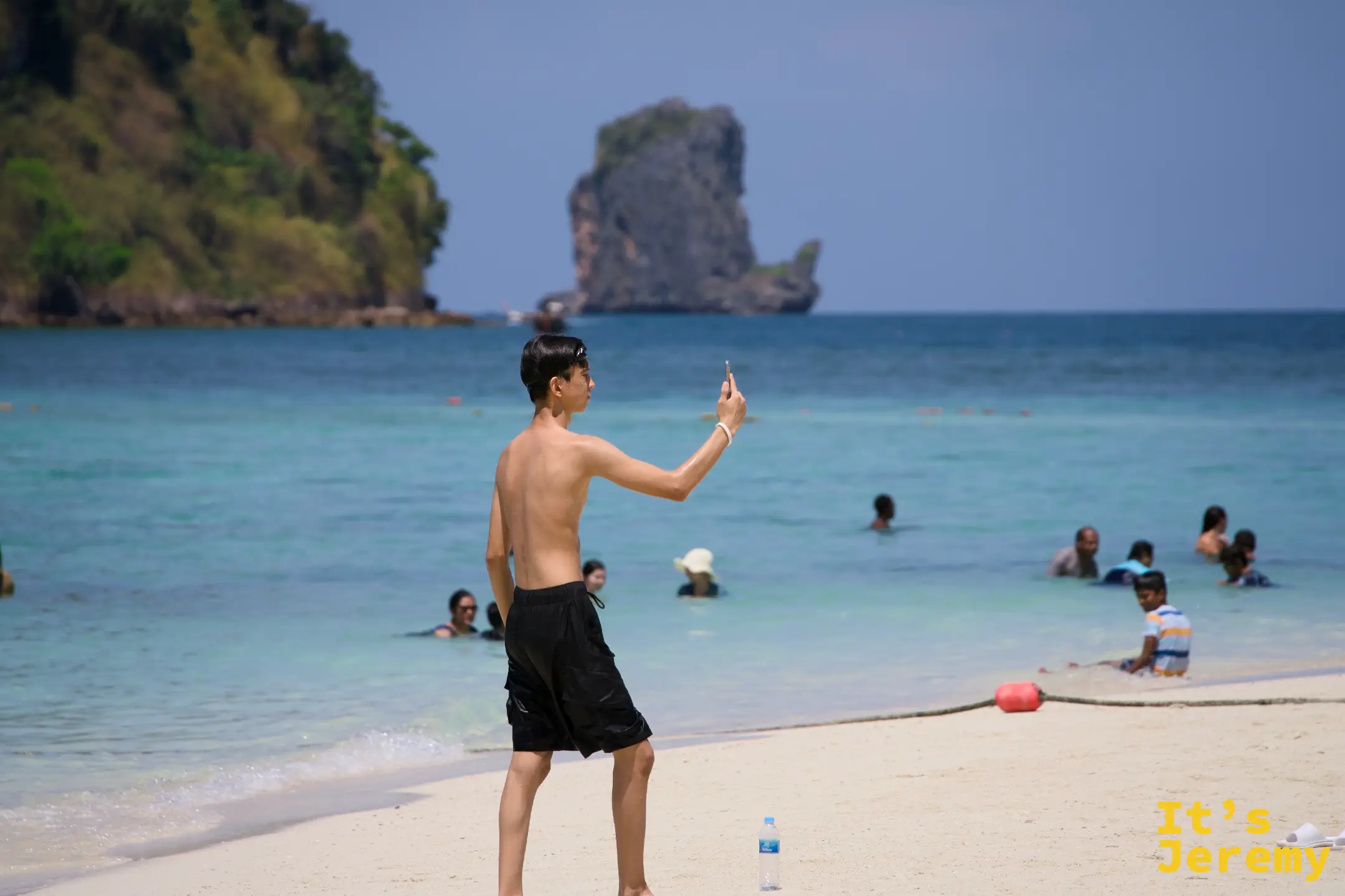 遊客在海灘上自拍，背後是一座突出海面的孤立石灰岩岩柱
