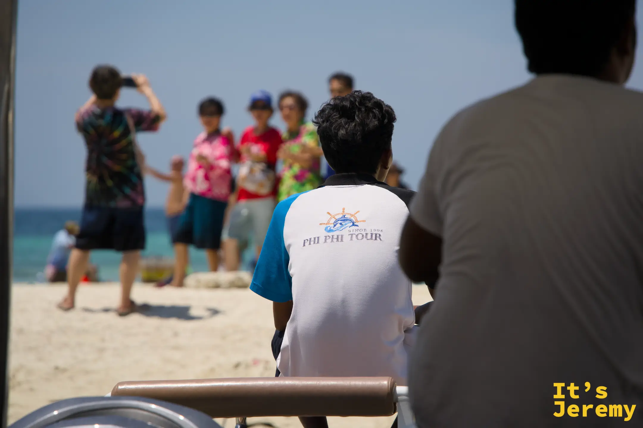 從船艙往外看，PHI PHI TOUR 導遊背對鏡頭，前方沙灘上旅客正在拍照