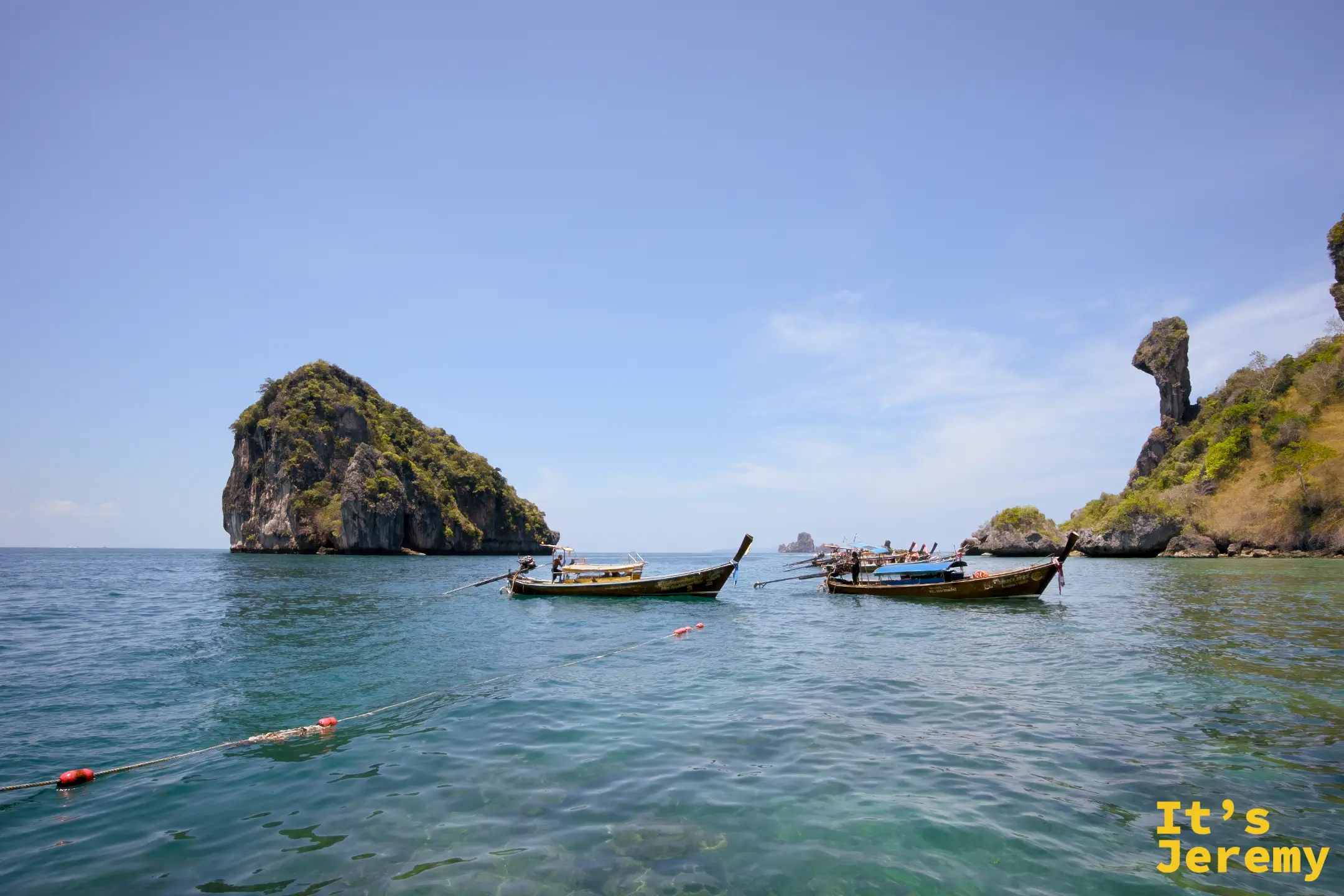 多艘長尾船在 Koh Si 旁的翡翠海面上並排停靠，遠處另一座石灰岩小島清晰可見