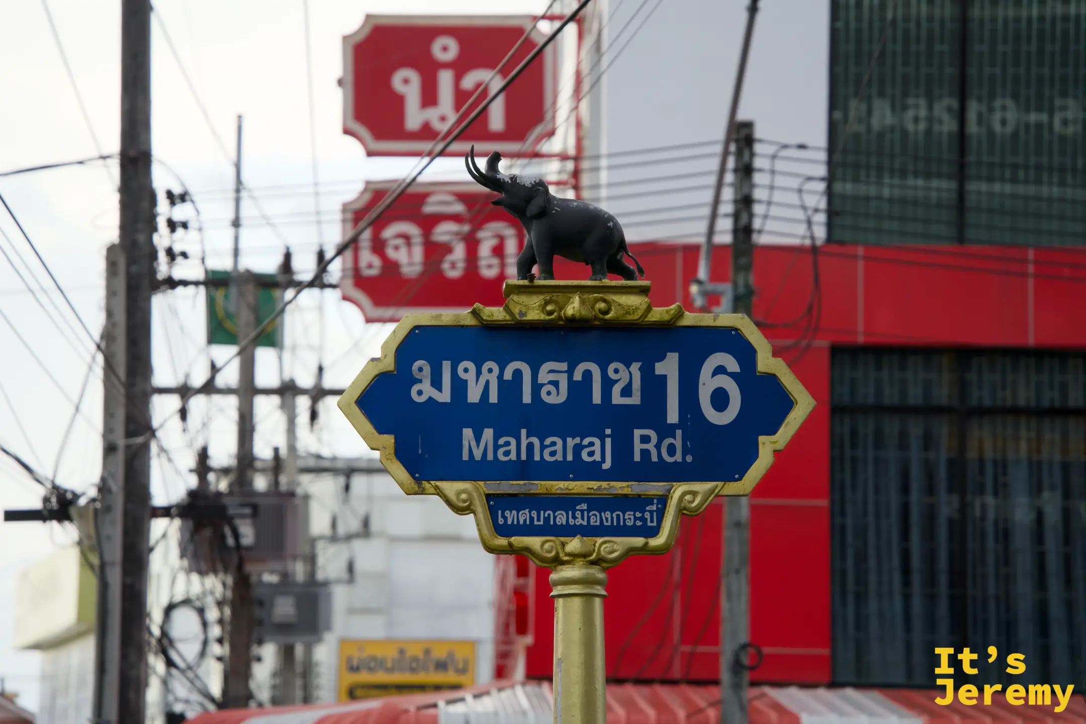 Maharaj Road 金框路牌特寫，頂端有象雕塑，背景是傍晚的市區街道