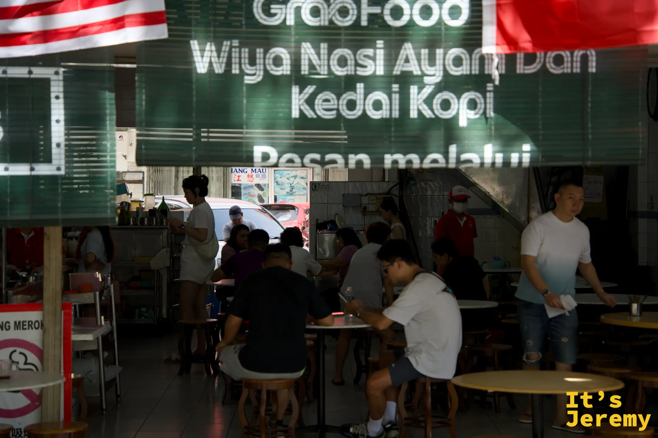 透過店面玻璃望進去，顧客坐滿，GrabFood 廣告貼在玻璃上，正中是備餐區