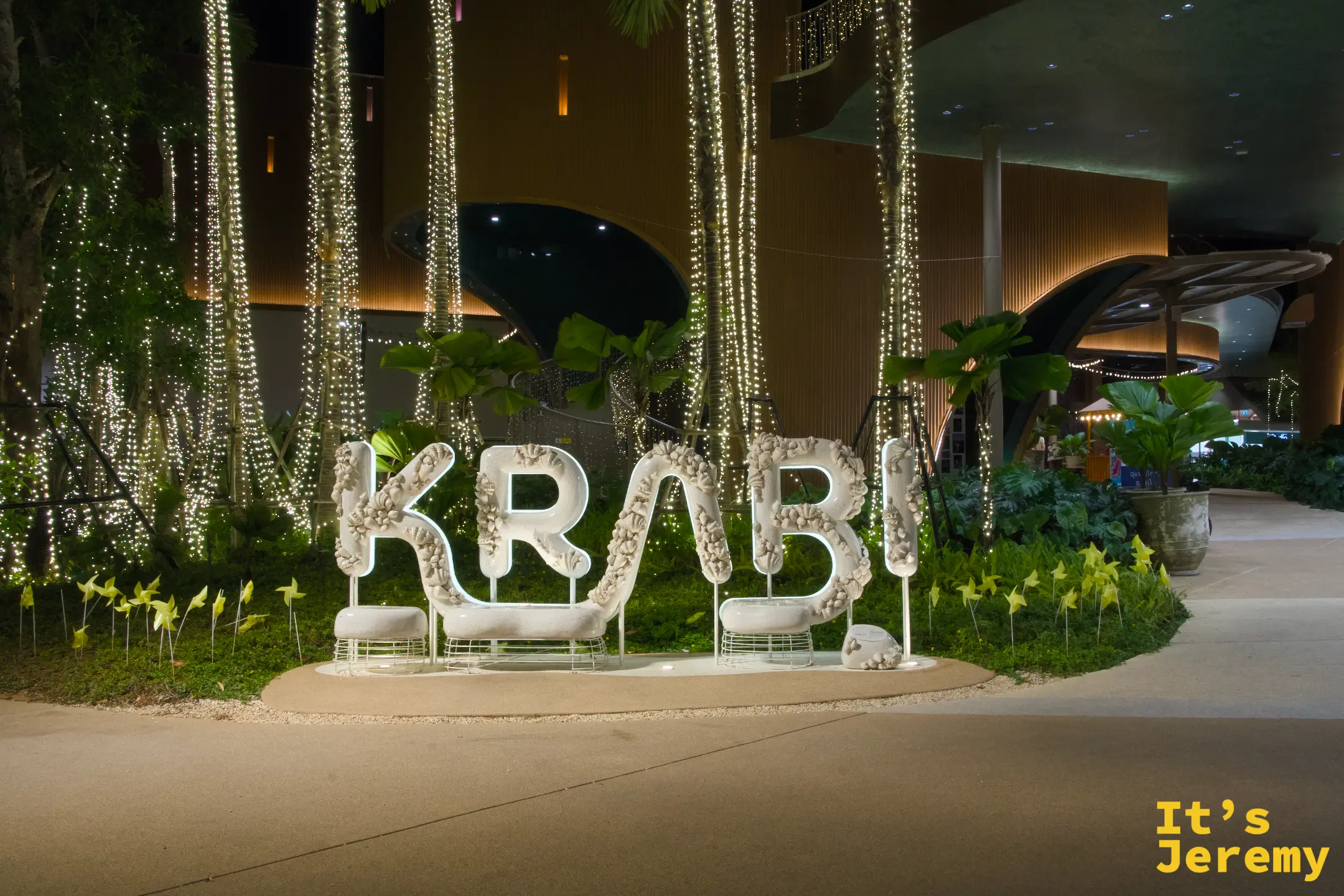 白色珊瑚貝殼造型的 KRABI 大字裝置,背後有燈光瀑布樹與綠色植栽