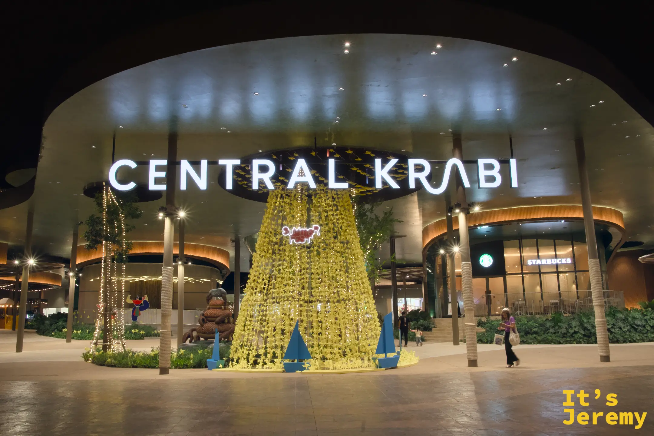 Central Krabi 正面外觀夜景，圓弧型建築打燈，入口前有黃色花瀑裝置，右側可見 Starbucks