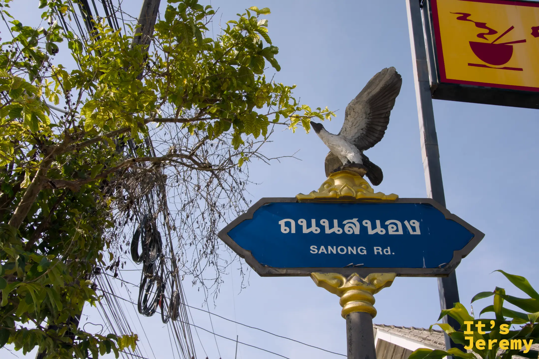 喀比市區 Sanong Rd. 路牌,藍色路牌頂端是一隻展翅的鷹形雕塑