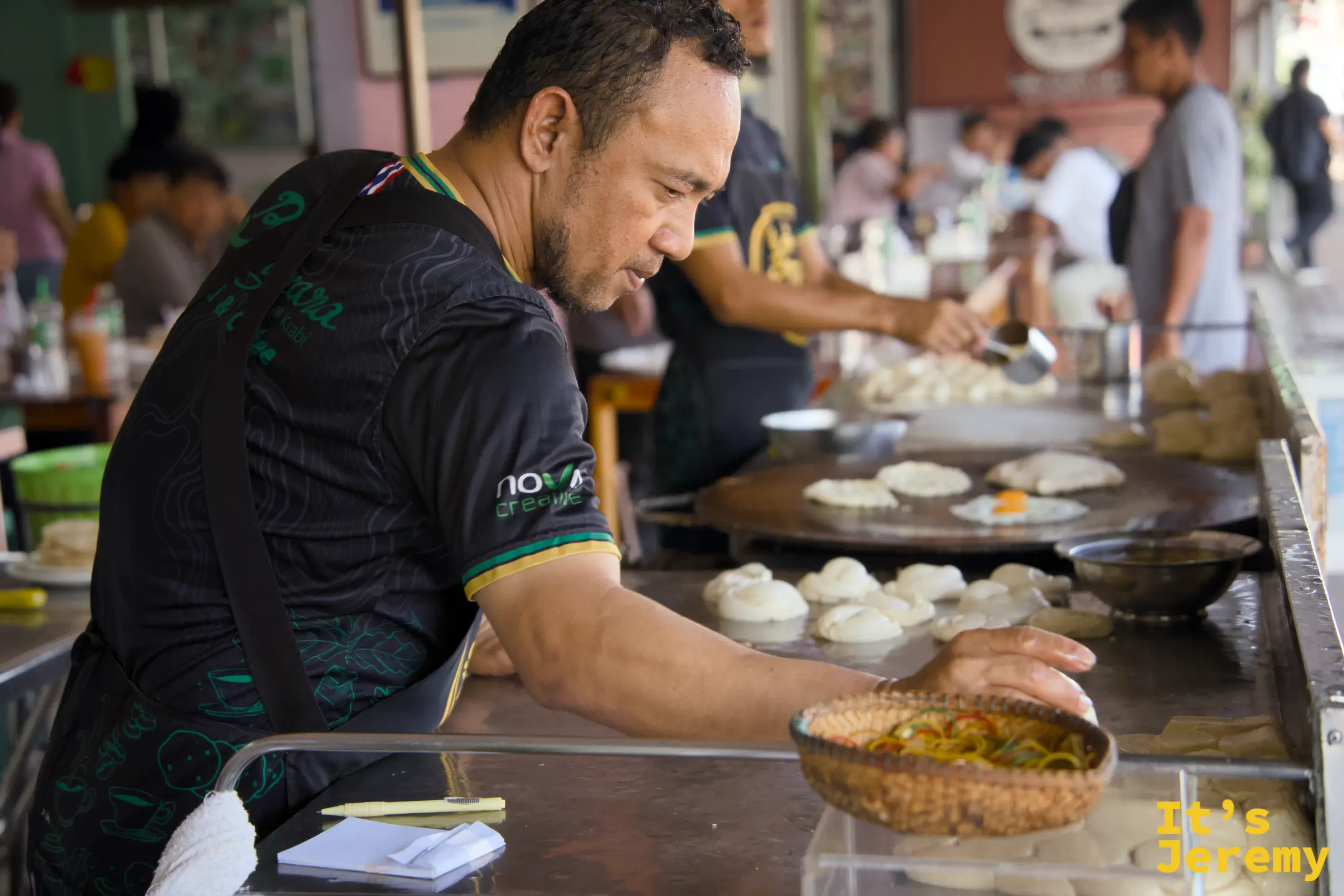 師傅雙手整理麵糰球，鐵板上同時煎著多張 Roti